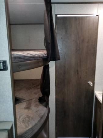 Compact sleeping area in an RV rental, featuring bunk beds, a privacy curtain, and a wood door.. Jayco Jay Flight SLX 2022