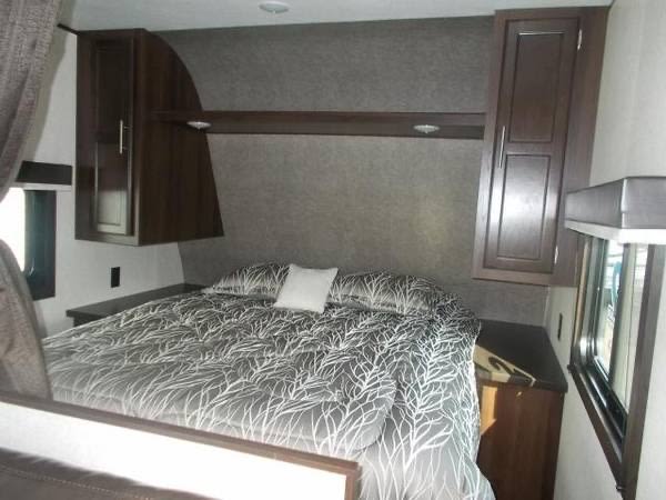 Cozy RV rental bedroom featuring dark wood cabinets, a grey and white patterned bed, and a window. Ideal for travel.. Jayco Jay Flight SLX 2022