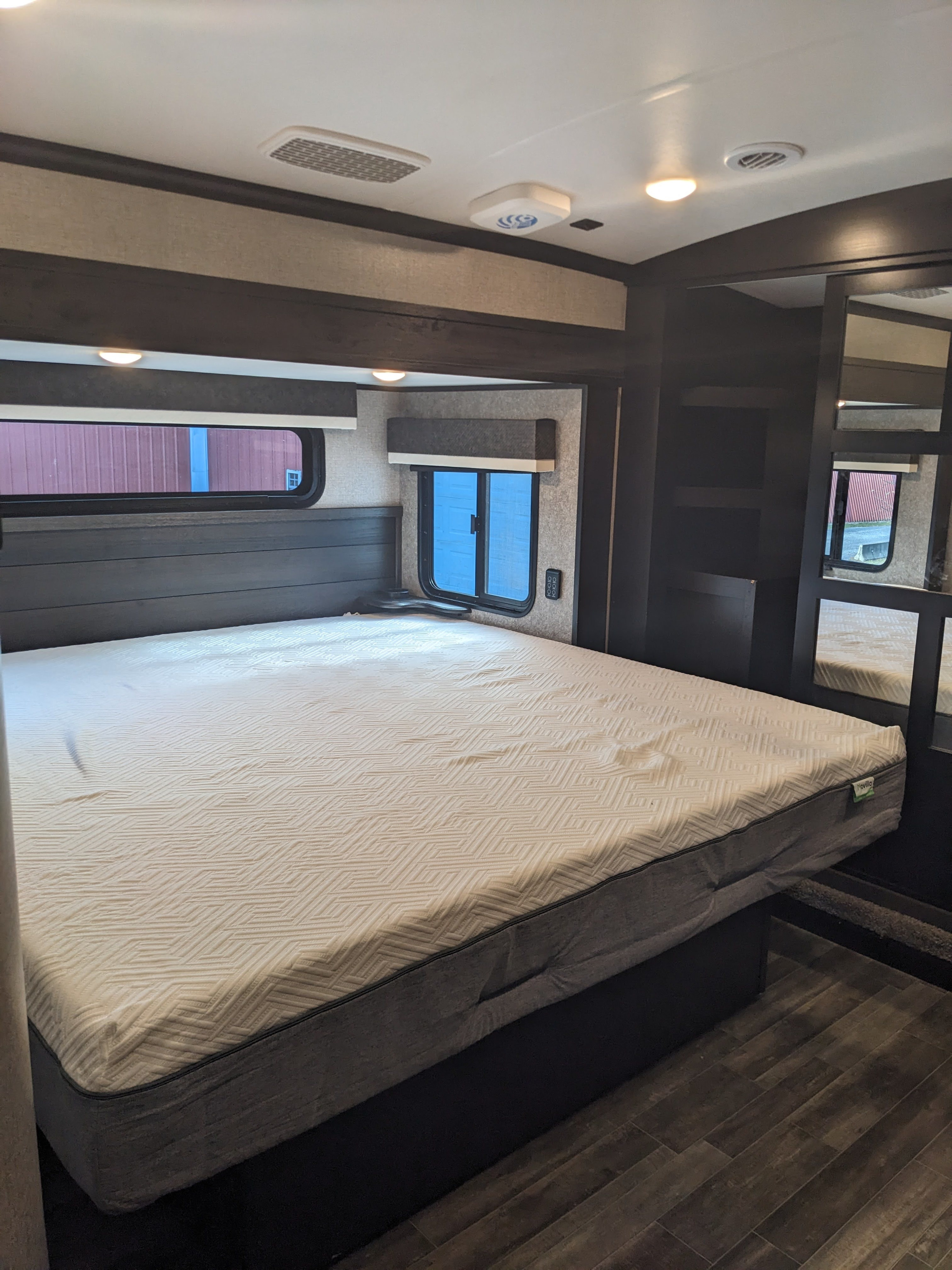 Comfortable RV rental bedroom showcasing a large mattress, dark wood headboard, and modern interior design.. Jayco North Point 2021