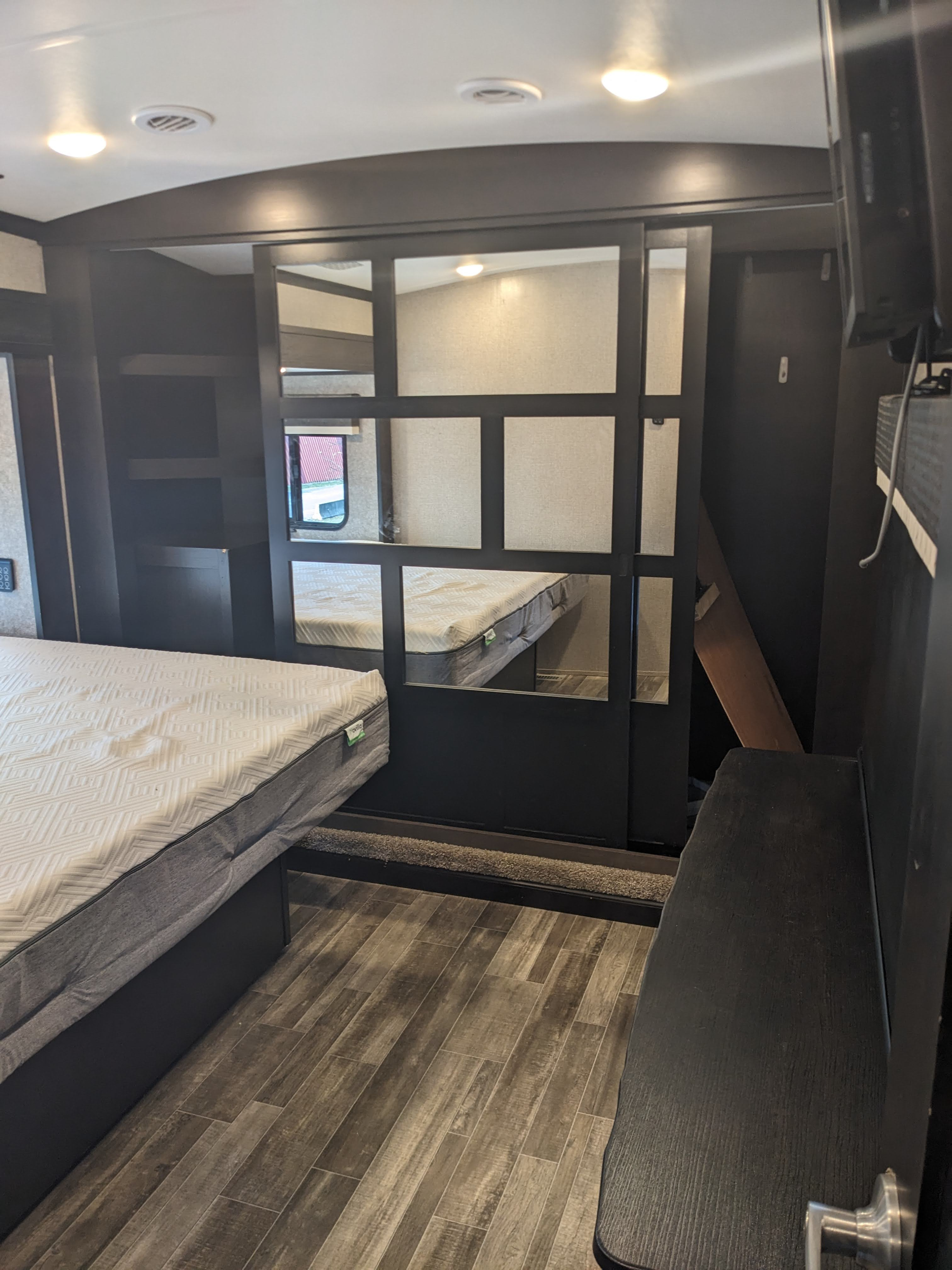 Inside a comfortable RV rental bedroom, showing a main bed, wood-look flooring, and a separate bunk area.. Jayco North Point 2021