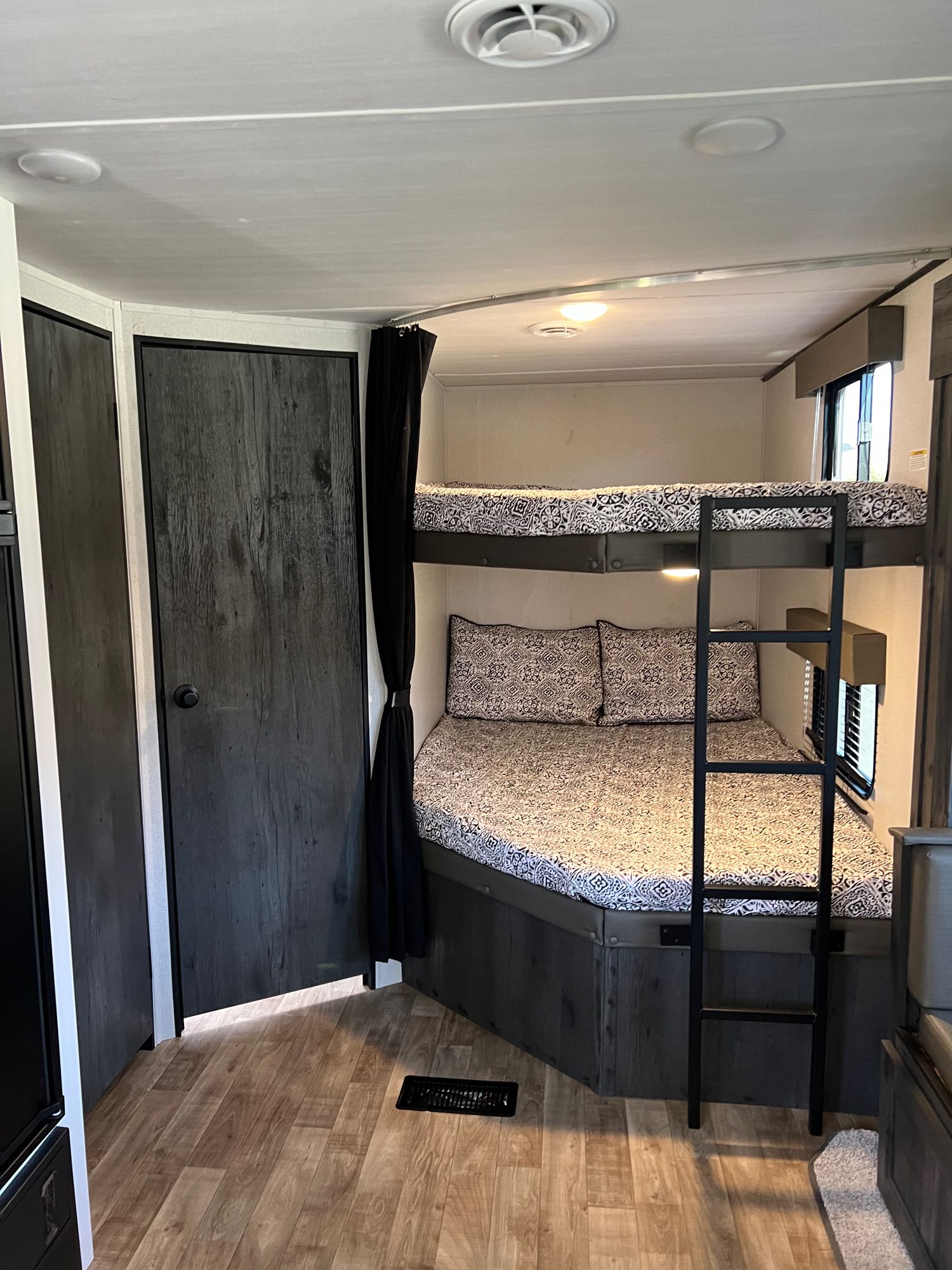 RV rental with inviting bunk beds featuring patterned bedding, a black ladder, dark doors, and light wood flooring for cozy stays.. Keystone RV Hideout 2023