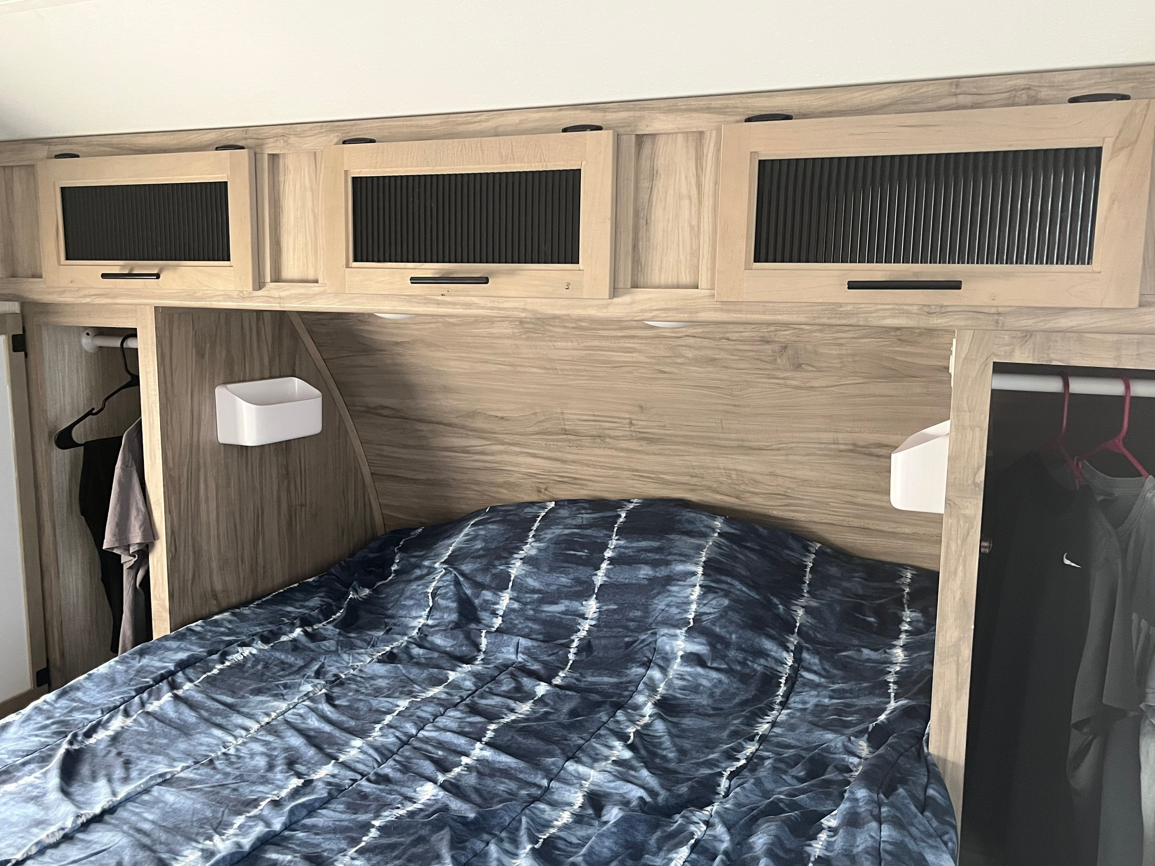 Compact RV rental bedroom featuring a blue patterned bed, overhead storage cabinets, and side hanging closets.. Forest River Cherokee Alpha Wolf 2021