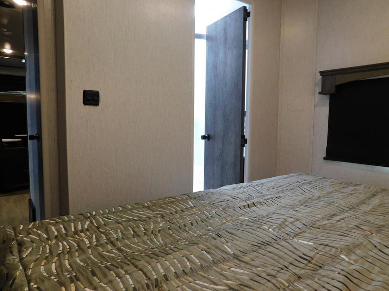 Cozy RV rental bedroom featuring a patterned comforter on the bed, a light switch, and open doors to the rest of the interior.. Forest River Shockwave 2022