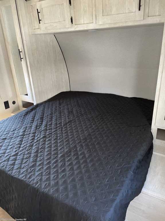 Modern RV rental bedroom featuring a spacious bed with quilted cover, overhead cabinets, and built-in wardrobe.. Forest River Shasta 2022