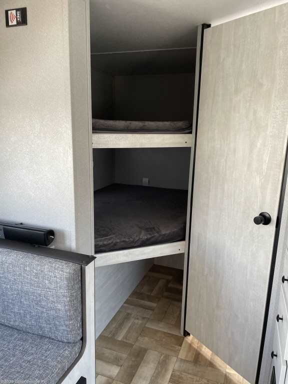 RV rental interior: two bunk beds, a grey cushioned seating area, and a partially open door. Features wood-look floor.. Forest River Shasta 2022