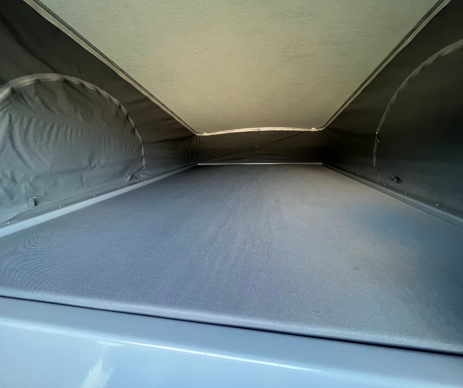 Inside a pop-top RV rental, showing the elevated sleeping platform with a light ceiling and dark fabric walls.. Winnebago 59PX 2021