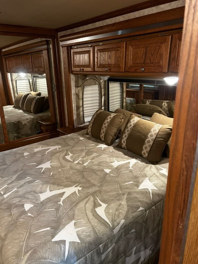 Inside an RV rental: a cozy bedroom with a bed featuring a gray leaf comforter, wood cabinets, and large mirrors, ideal for comfortable travel.. Allegro Allegro Bay 2006