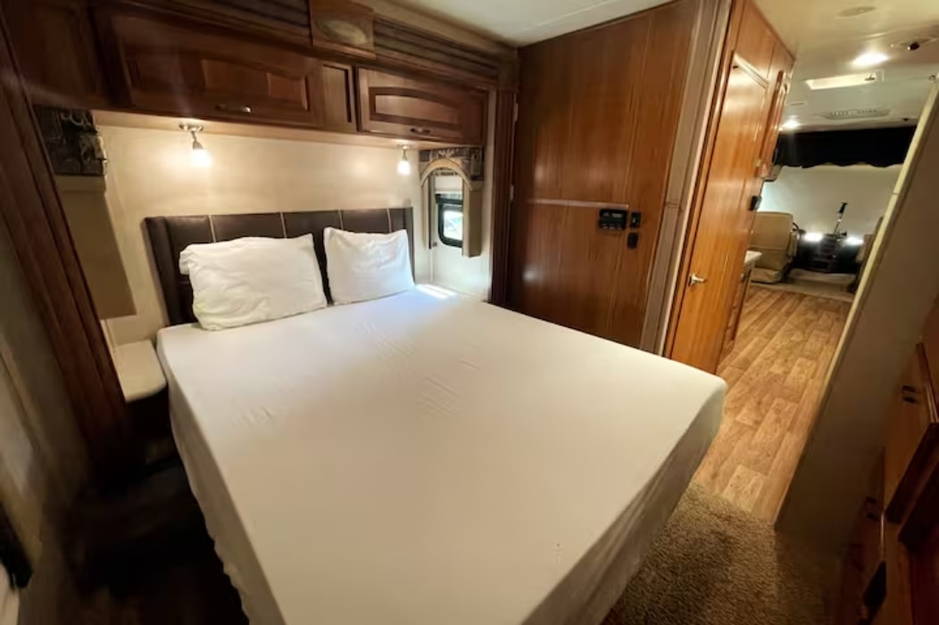 An RV rental's bedroom features a comfortable bed with white linens, wood cabinetry, and a clear path to the main living area.. Jayco Precept 2015
