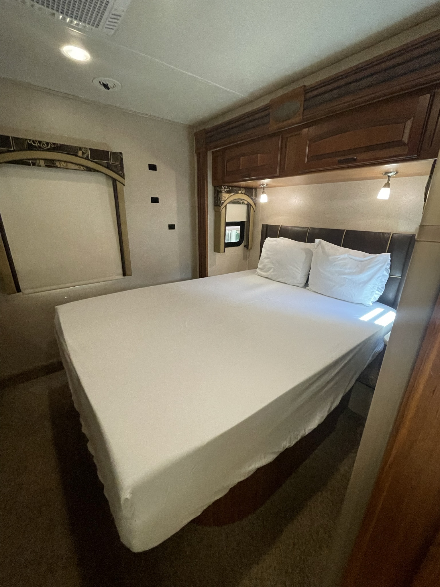 This clean RV rental bedroom offers a comfortable white-sheeted bed, brown headboard, and overhead storage.. Jayco Precept 2015