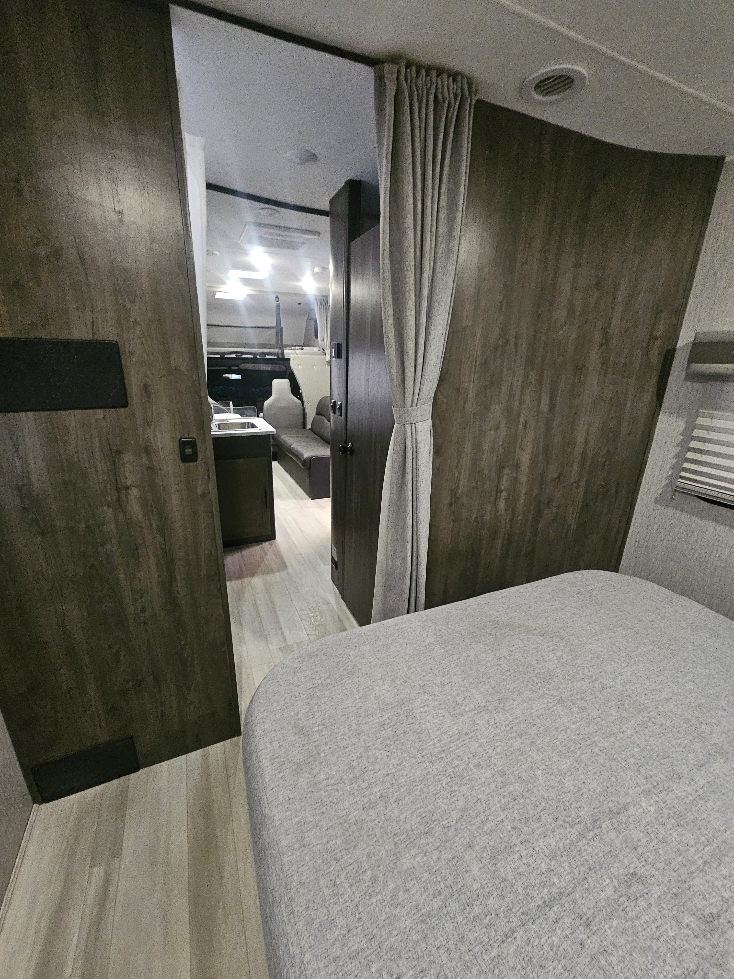 RV rental interior: cozy bedroom area with curtained privacy, leading to a compact kitchen and living space.. Coachmen Leprechaun 2022