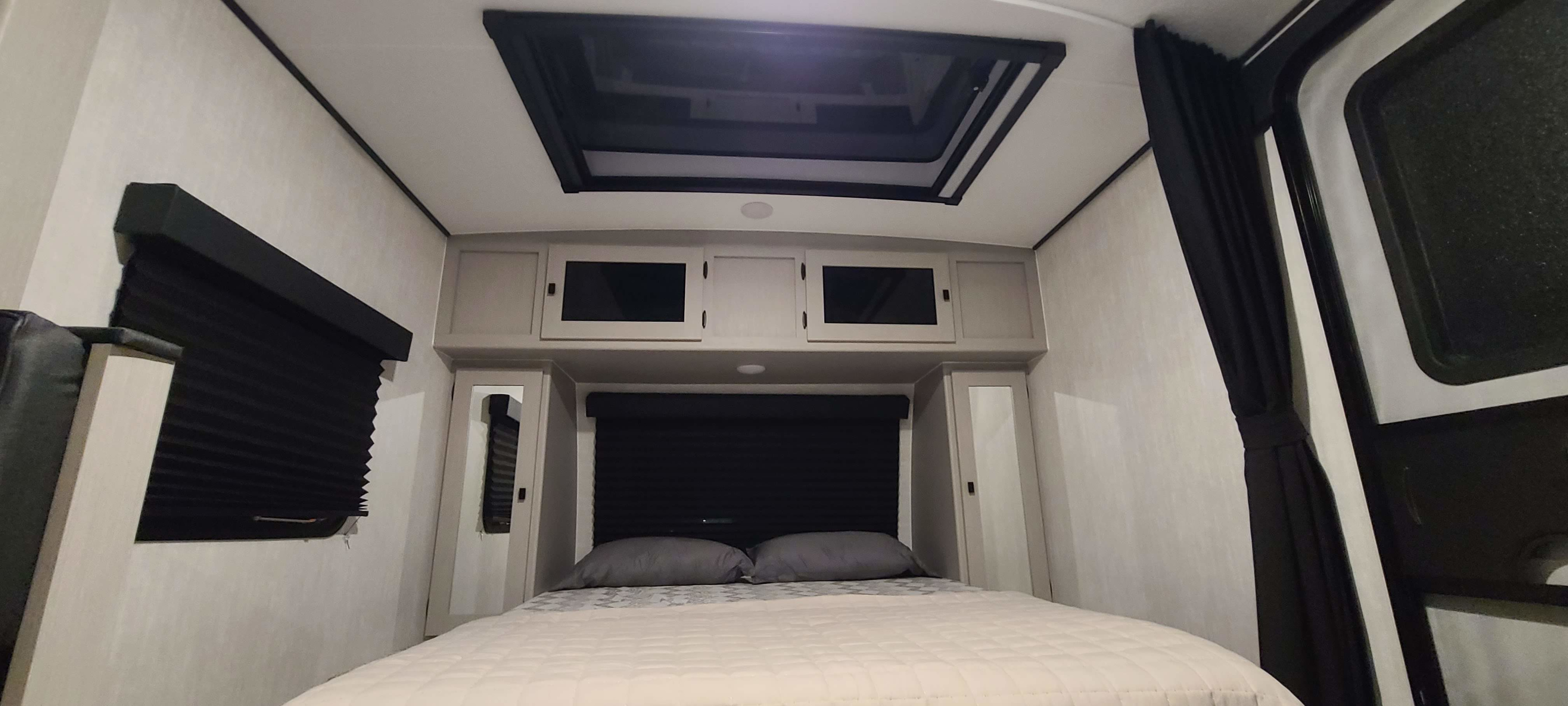 RV rental bedroom: bed, overhead cabinets, skylight, and dark pleated window blinds.. Forest River inc Apex 208 BHS 2024