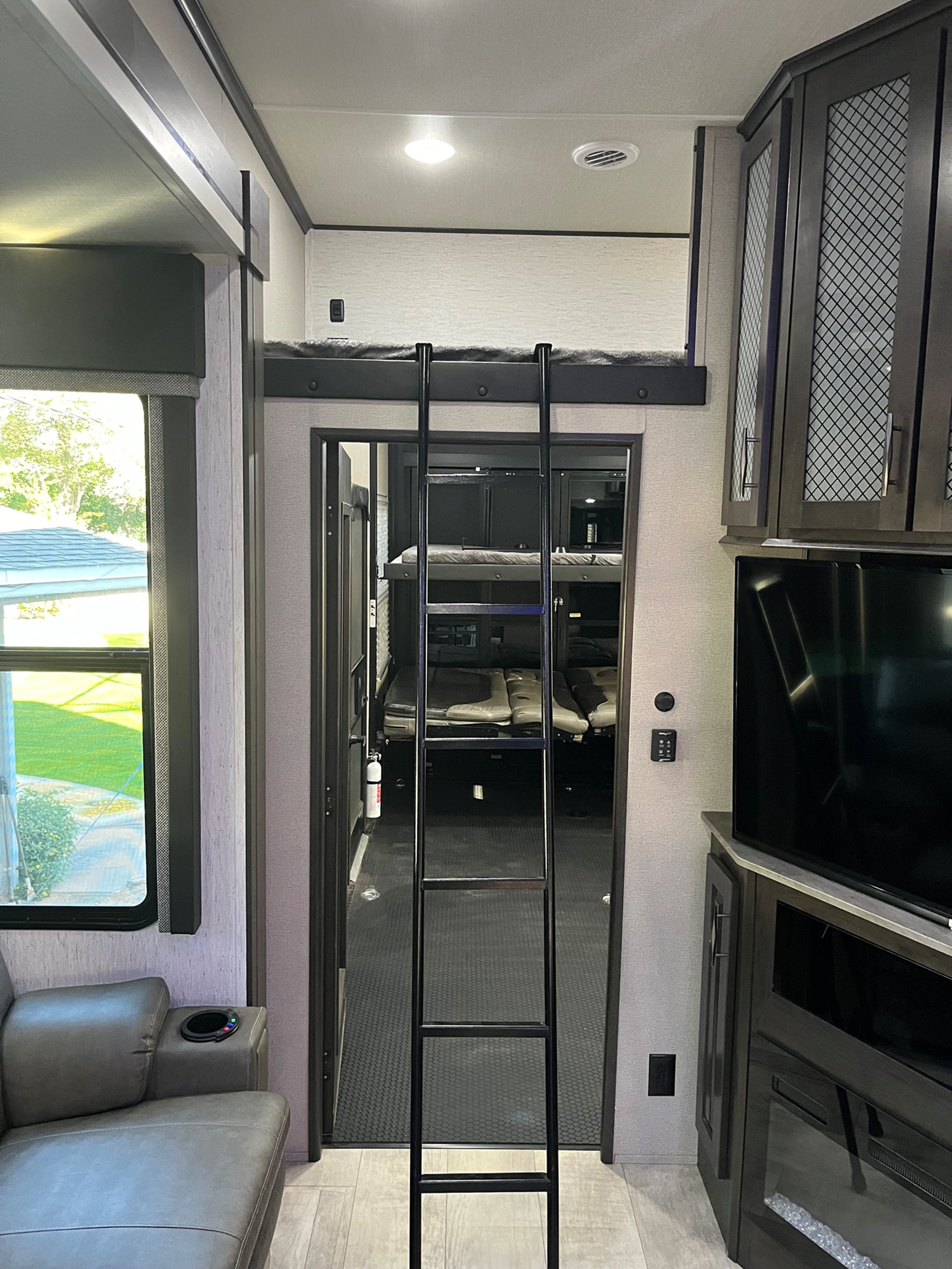 RV rental interior: living area with couch & TV, leading to a ladder and elevated bunk, plus a spacious rear garage/bunk room.. Grand Design Momentum M-Class Toy Hauler 2022