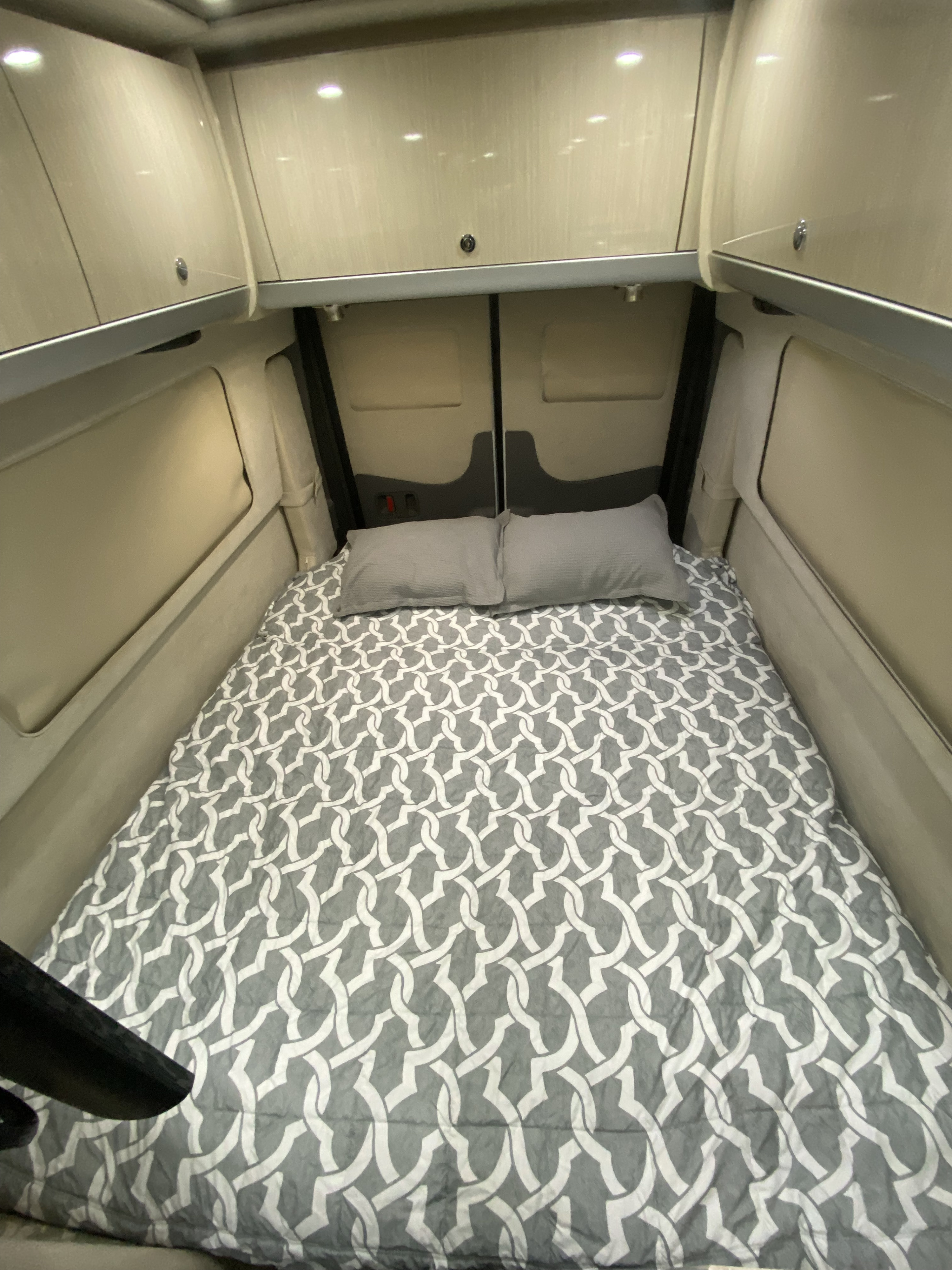 Cozy RV rental sleeping area featuring a bed with grey patterned bedding, pillows, and overhead storage cabinets.. Airstream Interstate 2017