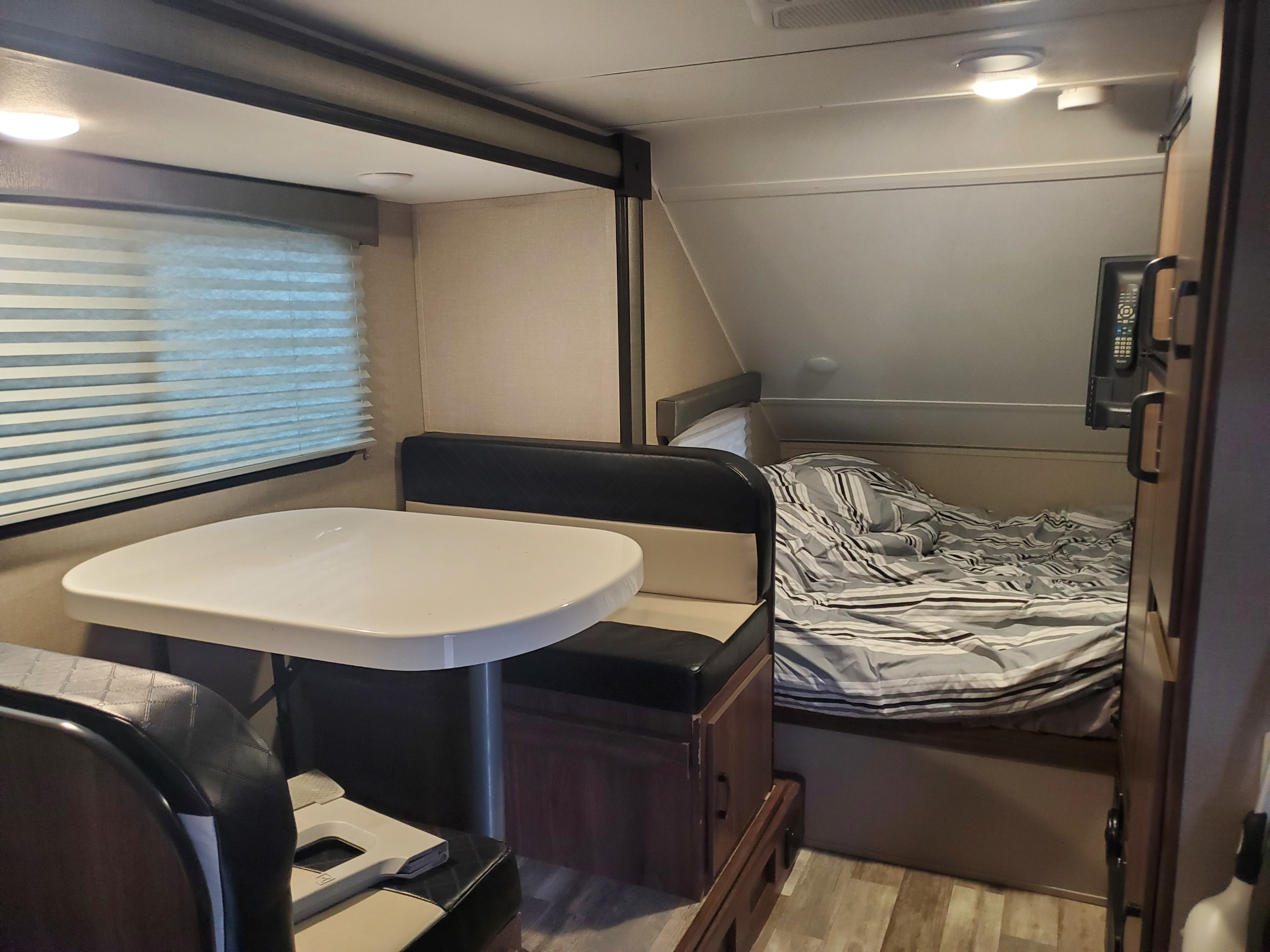 RV rental's inviting interior: dining booth, window with blinds, and cozy bed with striped bedding.. Travel Lite Aura 2020