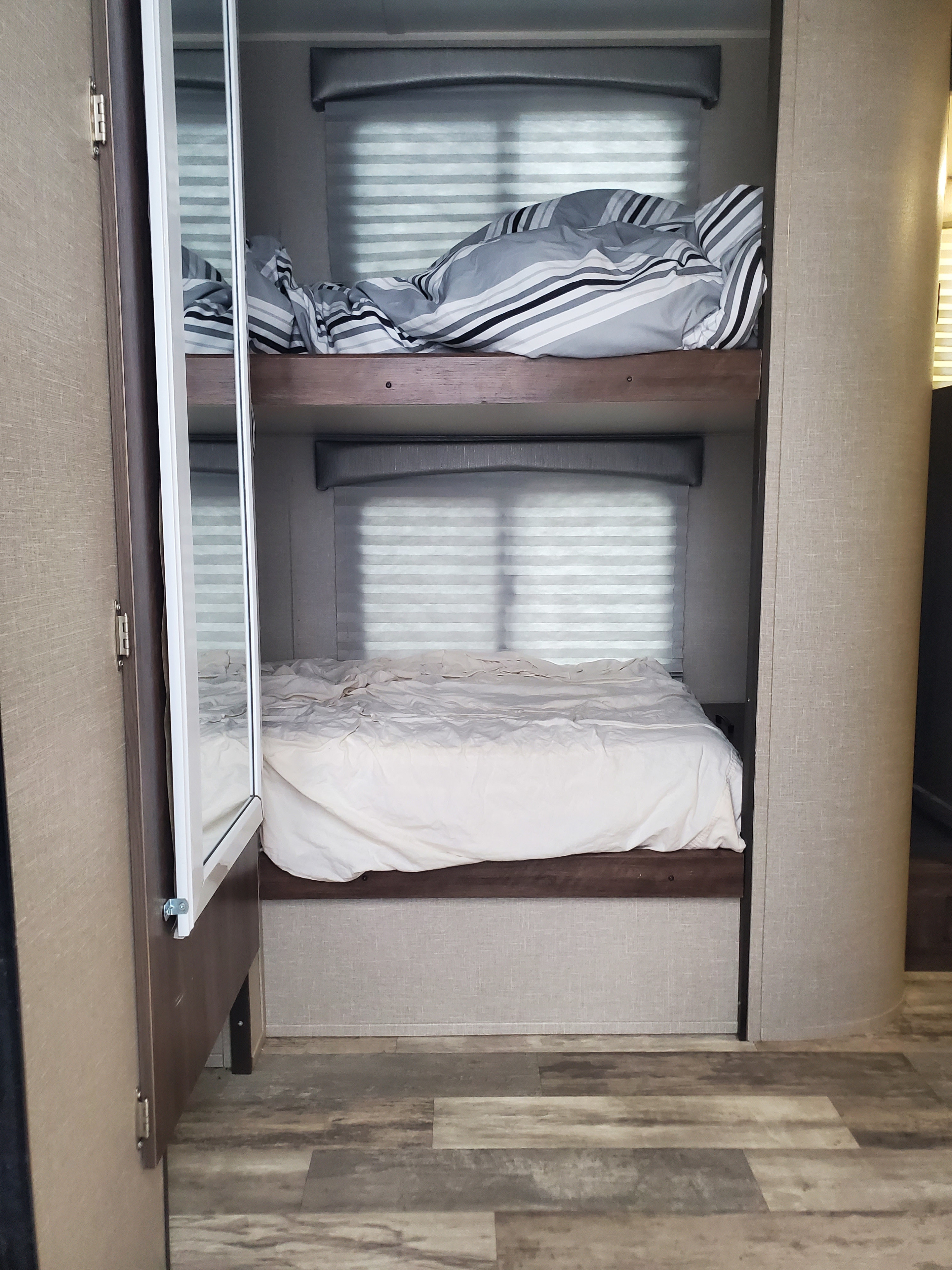 Inside an RV rental, showing neat bunk beds with striped and white bedding, perfect for comfortable travel.. Travel Lite Aura 2020