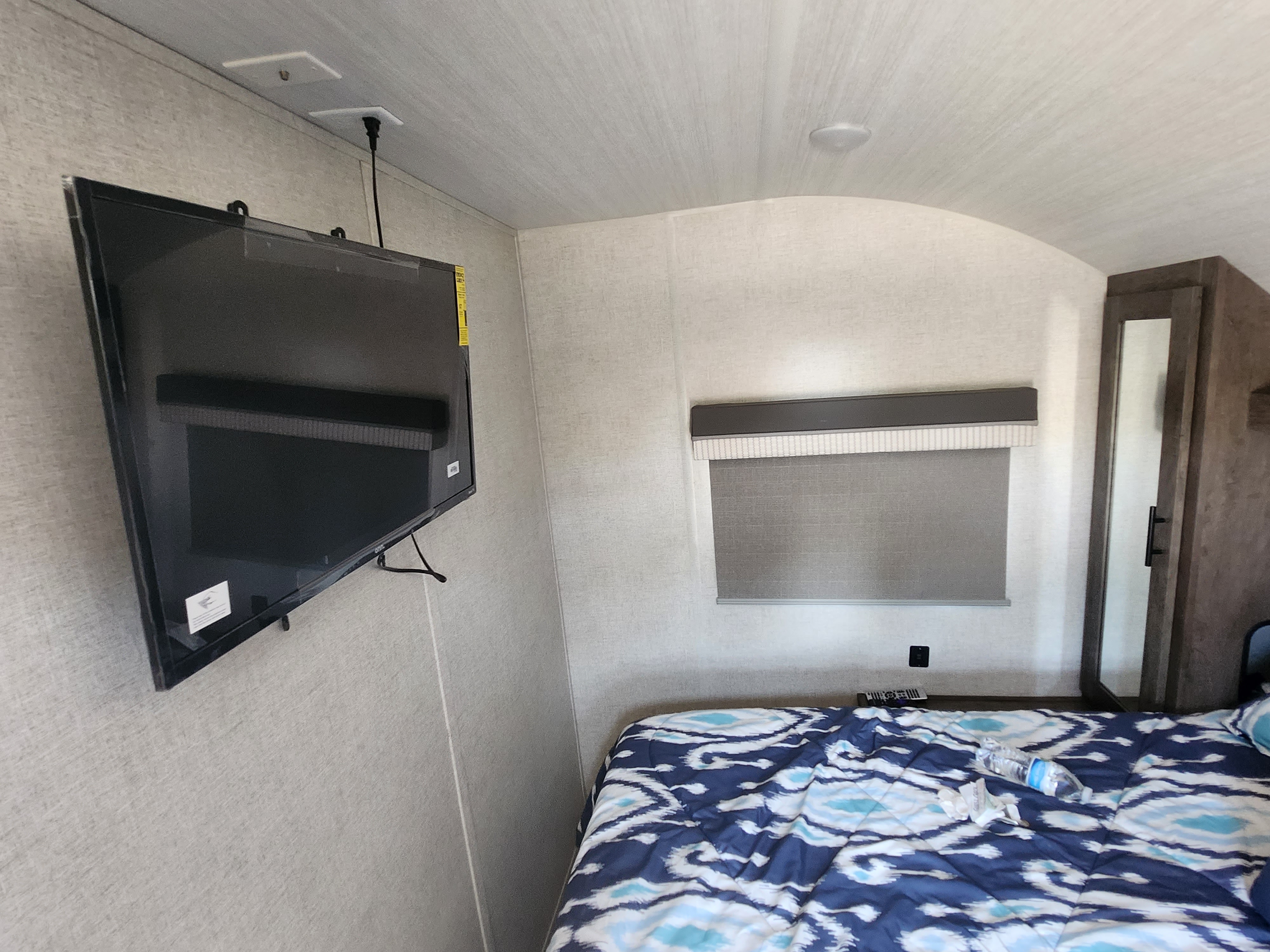 An RV rental bedroom features a wall-mounted TV, window with shade, and a bed with a blue patterned comforter.. Forest River Salem Cruise Lite 2021