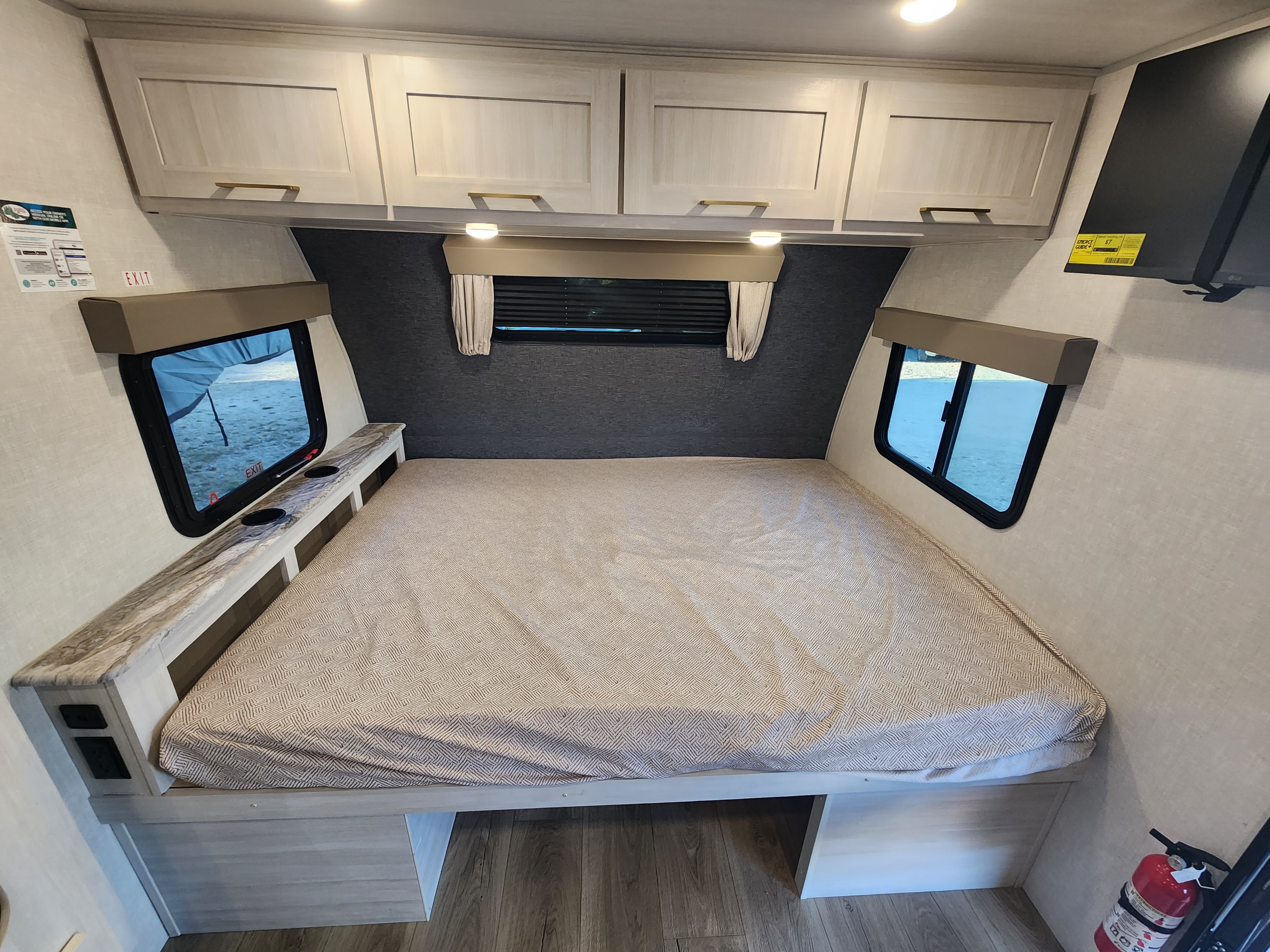 Spacious RV rental bedroom with a large bed, overhead cabinets, and dual windows for a comfortable night's sleep on your adventure.. Forest River Surveyor 19BHLE 2024