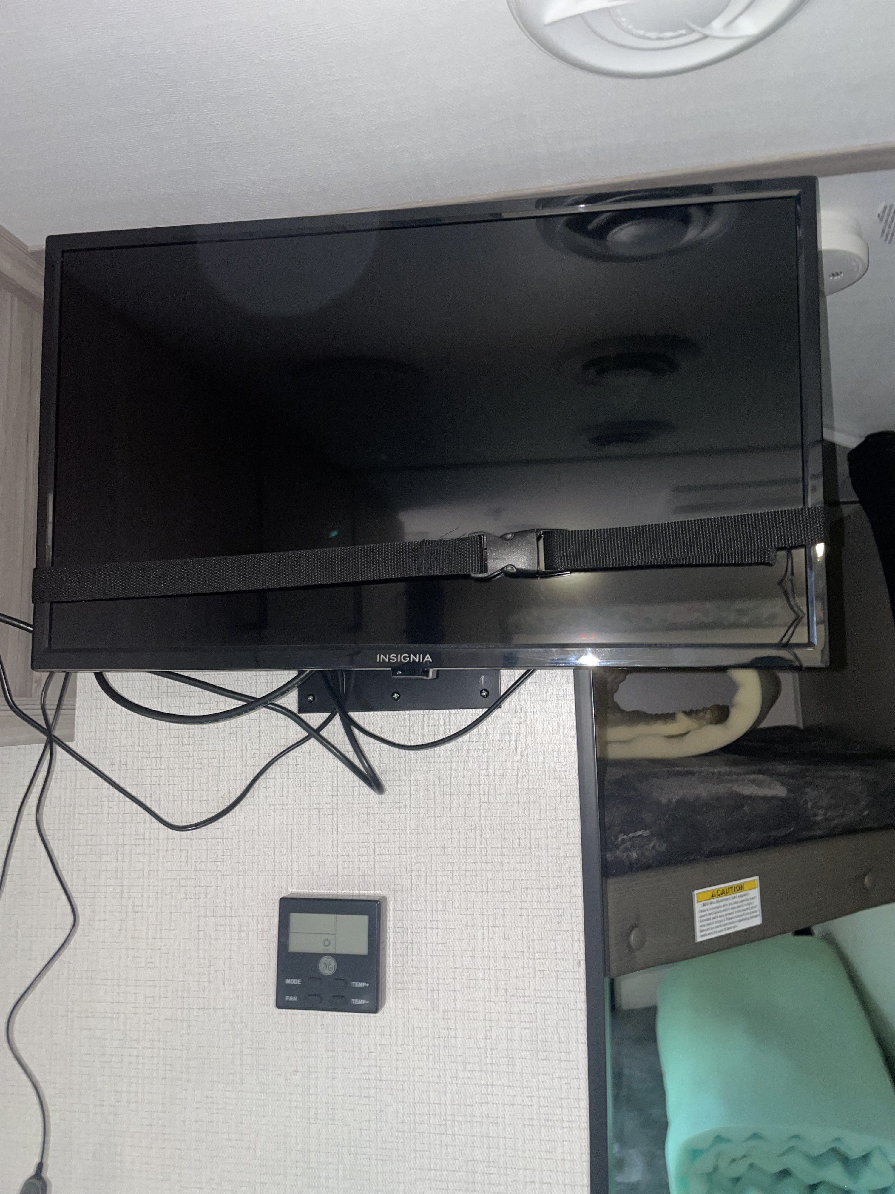 RV rental interior showing an Insignia TV, secured with a strap, mounted above a GE thermostat and bunk beds.. Keystone RV Passport SL 2022