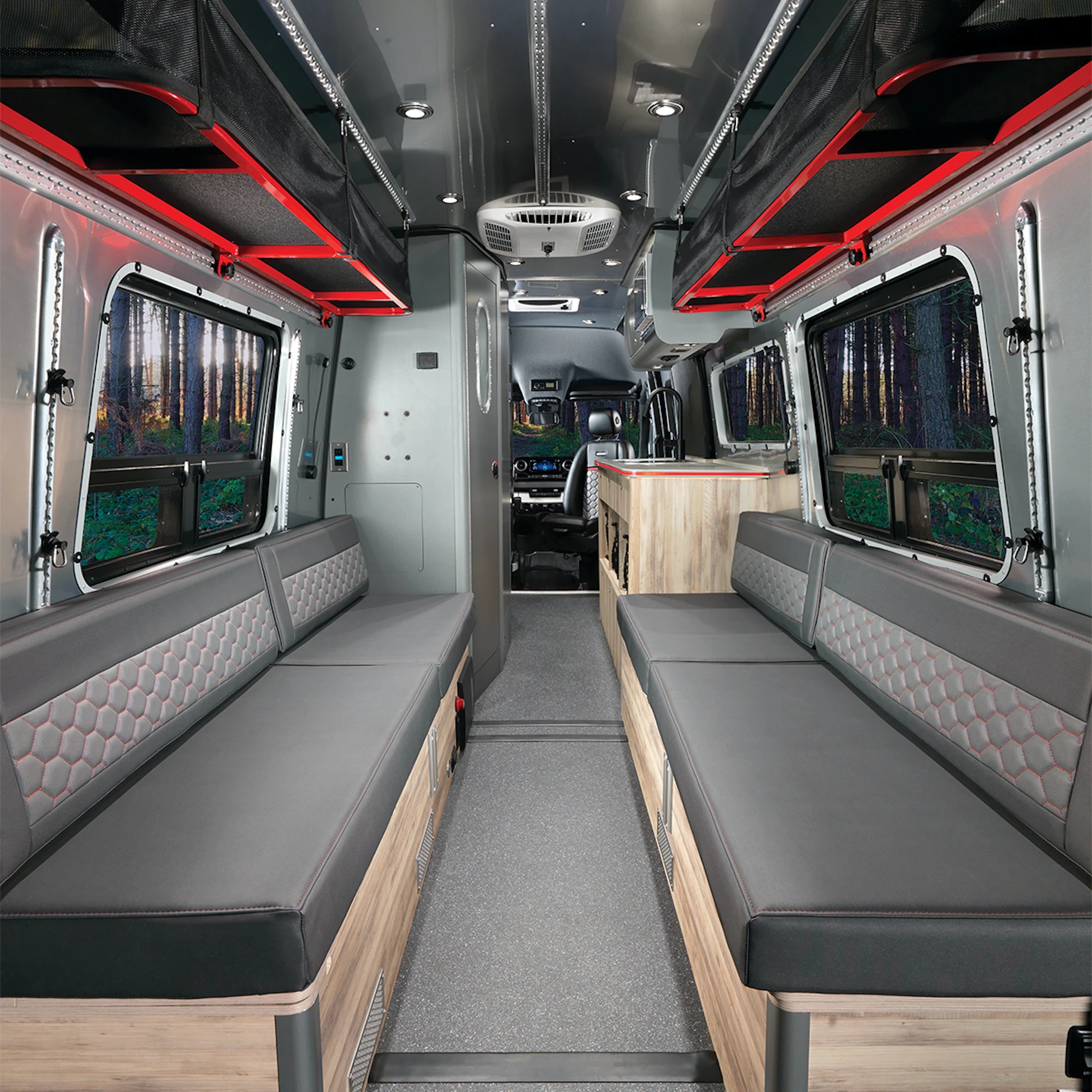 Explore this RV rental's spacious interior with comfy bench seats, overhead storage, and kitchen, offering great forest views.. Airstream Interstate 2022