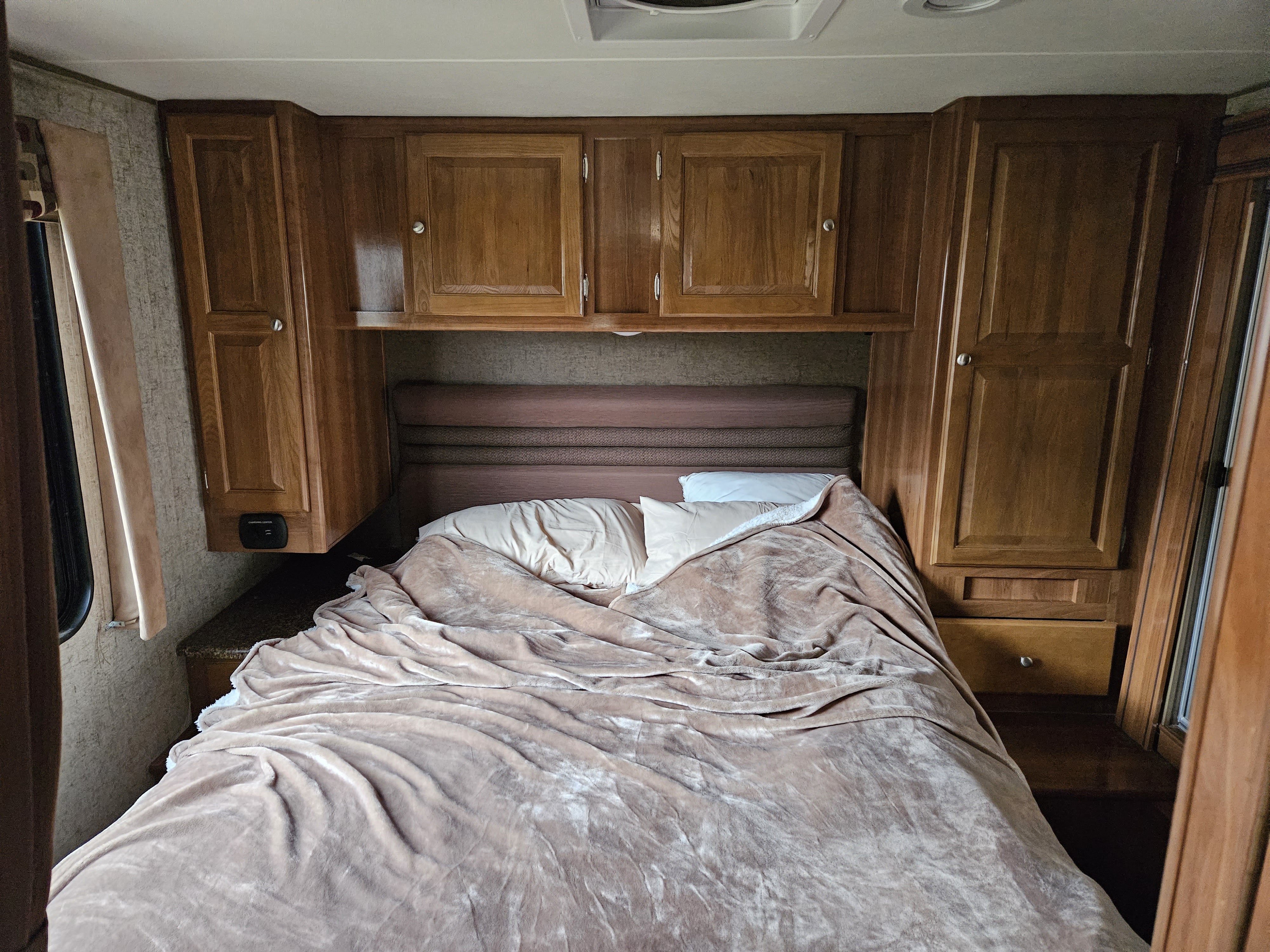 Inside an RV rental: a cozy bedroom featuring a bed with a soft blanket, wooden overhead cabinets, and built-in side storage.. COACHMEN Leprechaun 319MB 2017