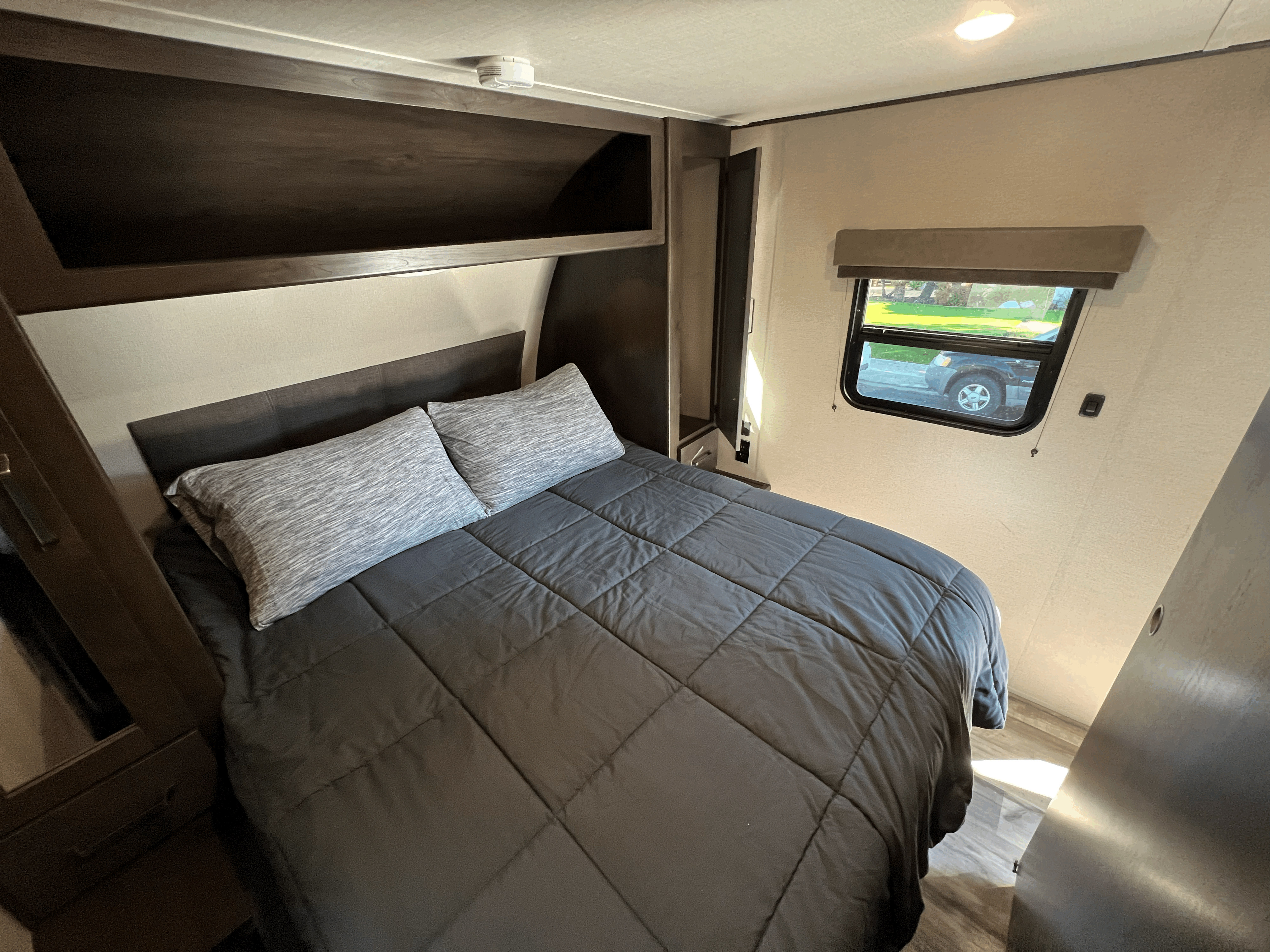 RV rental interior: Comfortable bedroom with dark gray bedding, overhead storage, and window views for your travel.. Grand Design Transcend Xplor 2022