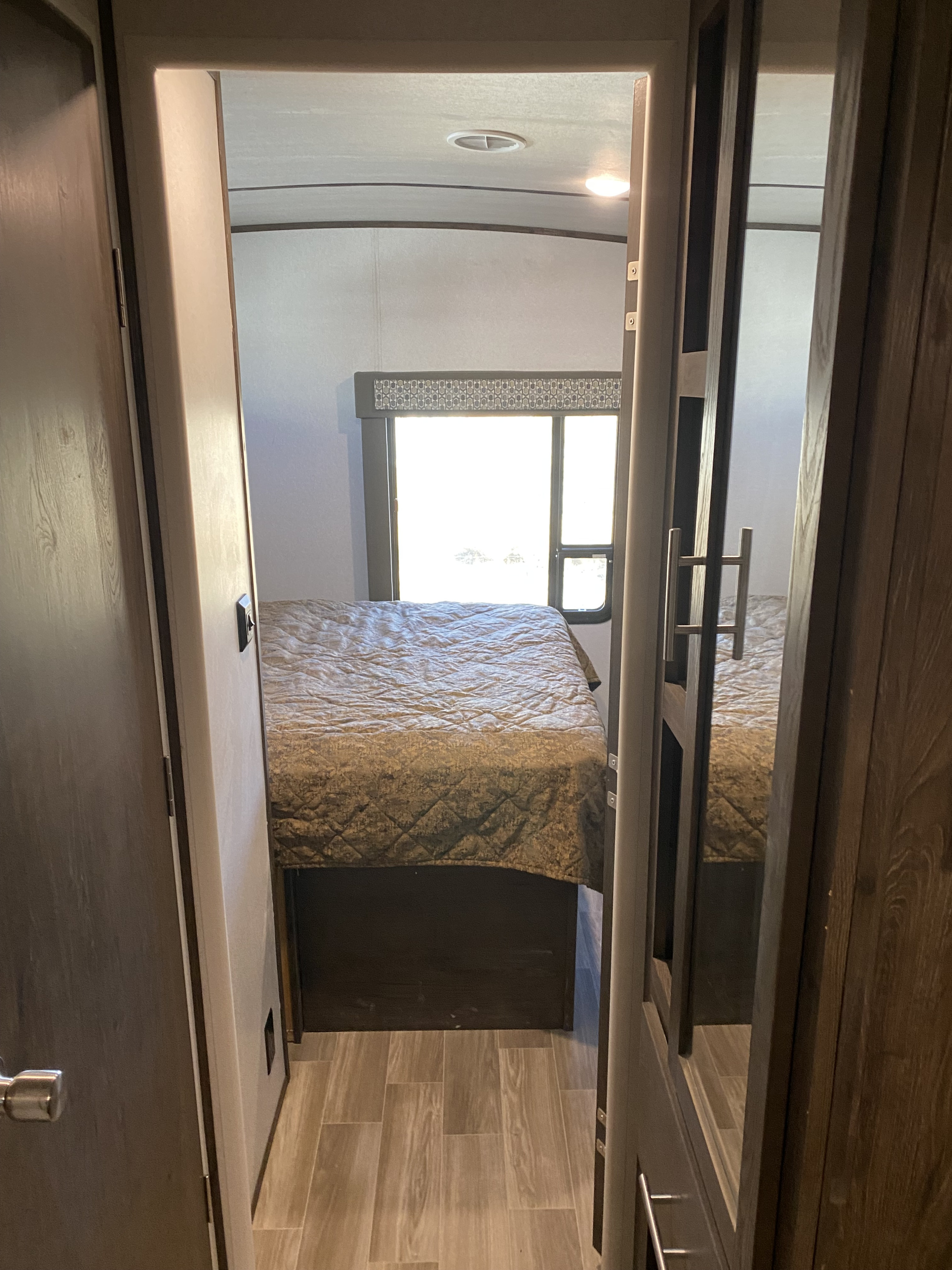 RV rental interior: bedroom with quilted bed, bright window, and mirrored closet door, viewed from doorway.. Forest River Salem Hemisphere GLX 2019
