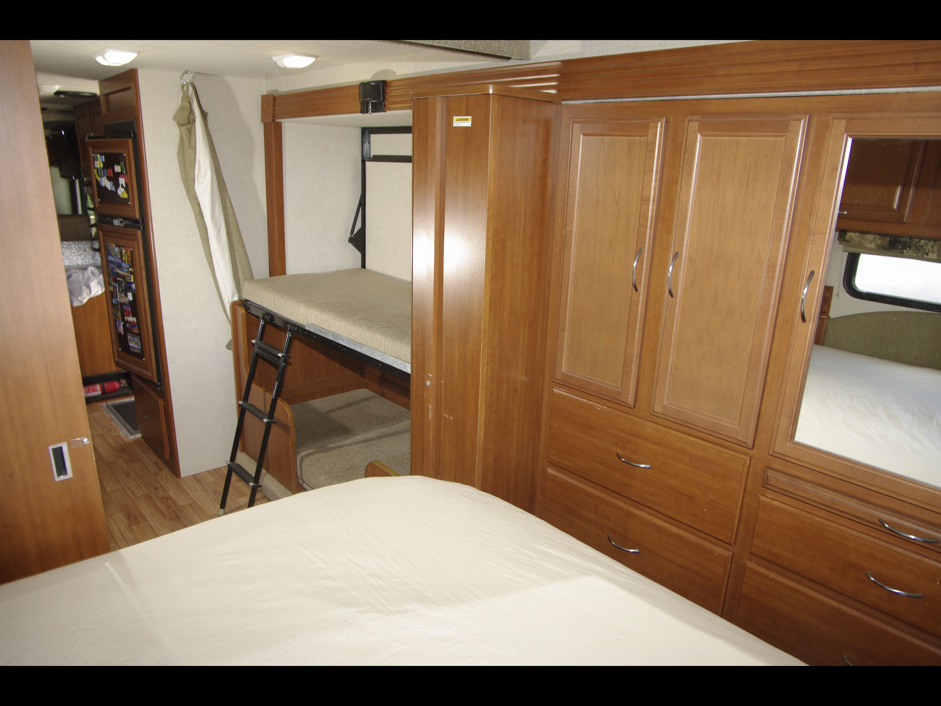 RV rental interior: bunk beds with ladder, main sleeping area, and extensive wood storage cabinets with mirror. Ideal for family travel.. Fleetwood Encounter 32BH 2010