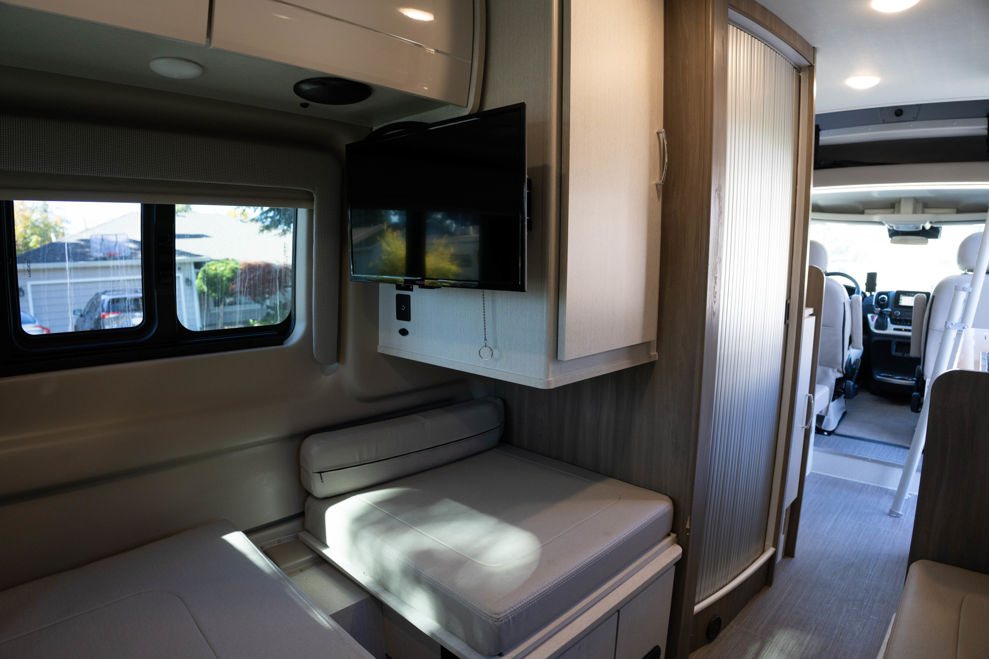 This rv rental's cozy interior features a comfortable seating area, a mounted TV, and a glimpse into the driver's cabin.. Thor Tellaro 2023