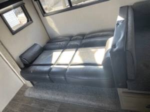 This RV rental's interior features an extended dark sleeper sofa (bed) in the bright living area, with sunlight streaming from windows.. Forest River Cherokee Alpha Wolf 2021