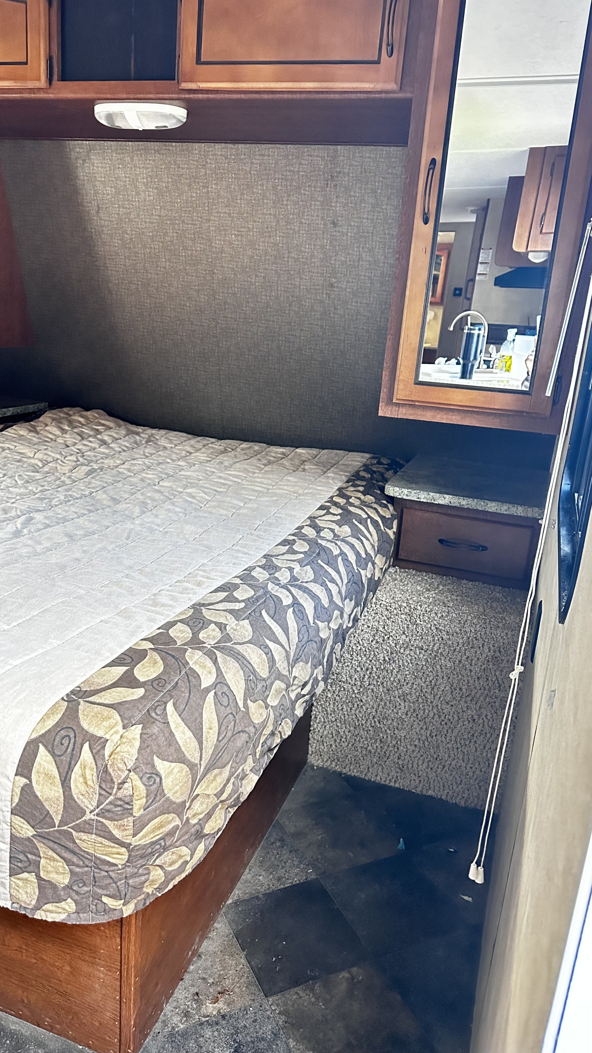 Cozy RV rental bedroom with patterned bedspread, overhead storage, and mirror reflecting kitchen.. Keystone RV Springdale 2014