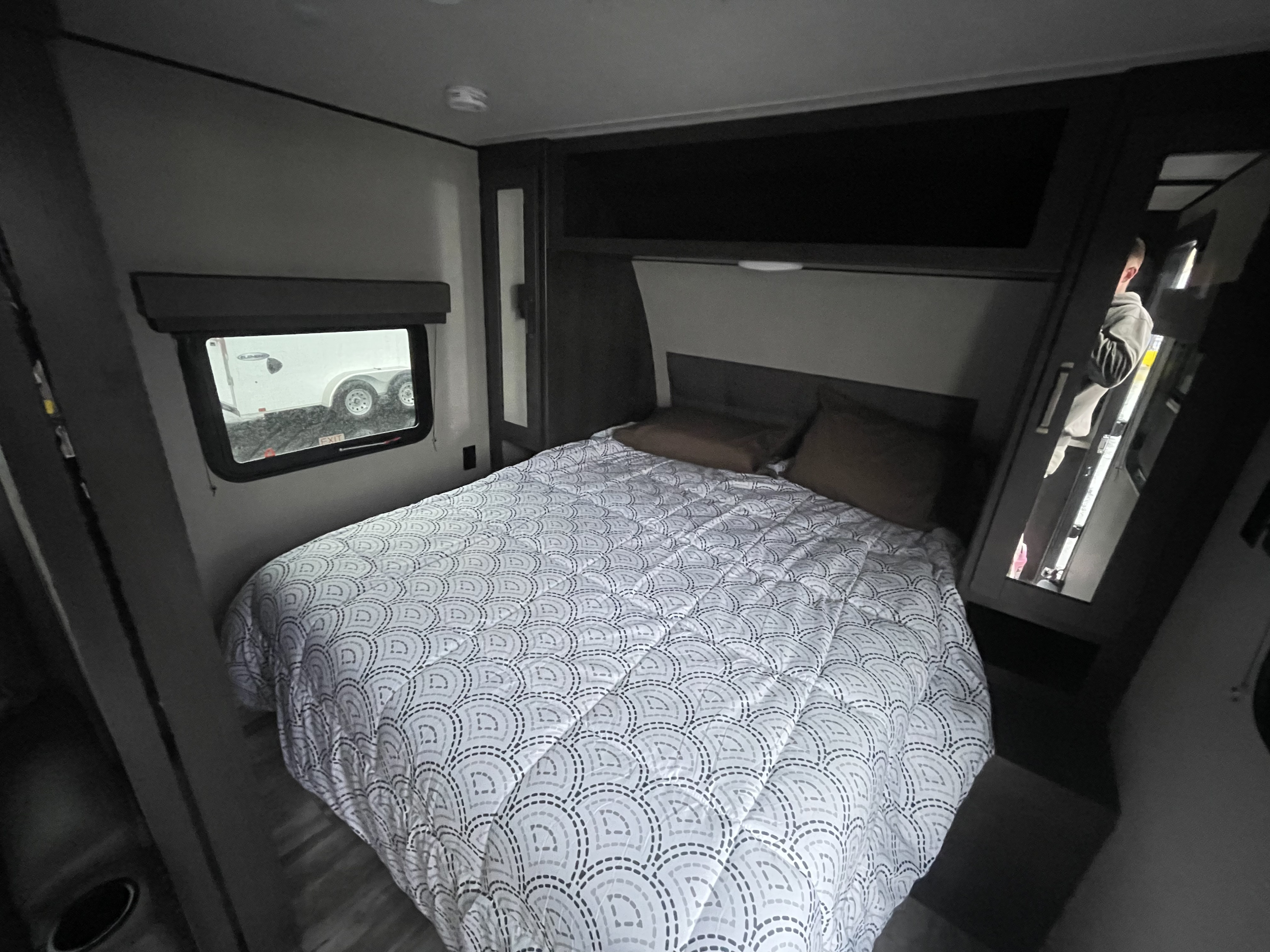 RV rental bedroom: a compact space featuring a patterned bed, brown pillows, a window, and a mirrored wardrobe.. Grand Design Transcend Xplor 2022