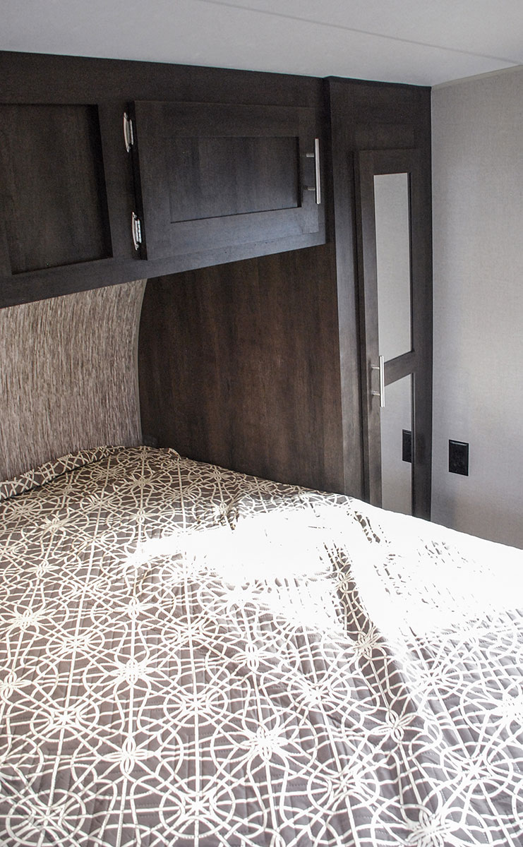 Cozy RV rental bedroom: dark wood cabinets, comfy bed with geometric pattern, and mirrored wardrobe.. K-Z Manufacturing Sportster 2019