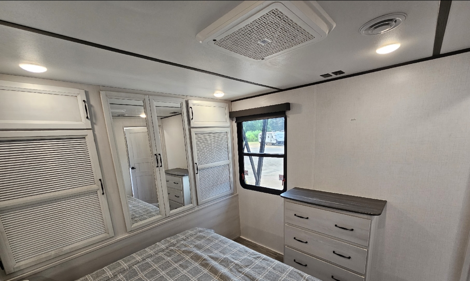 Modern RV rental bedroom: bed, mirrored closet, dresser, AC unit, and window offer comfort on the road.. Keystone Sprinter Wide Body 2023