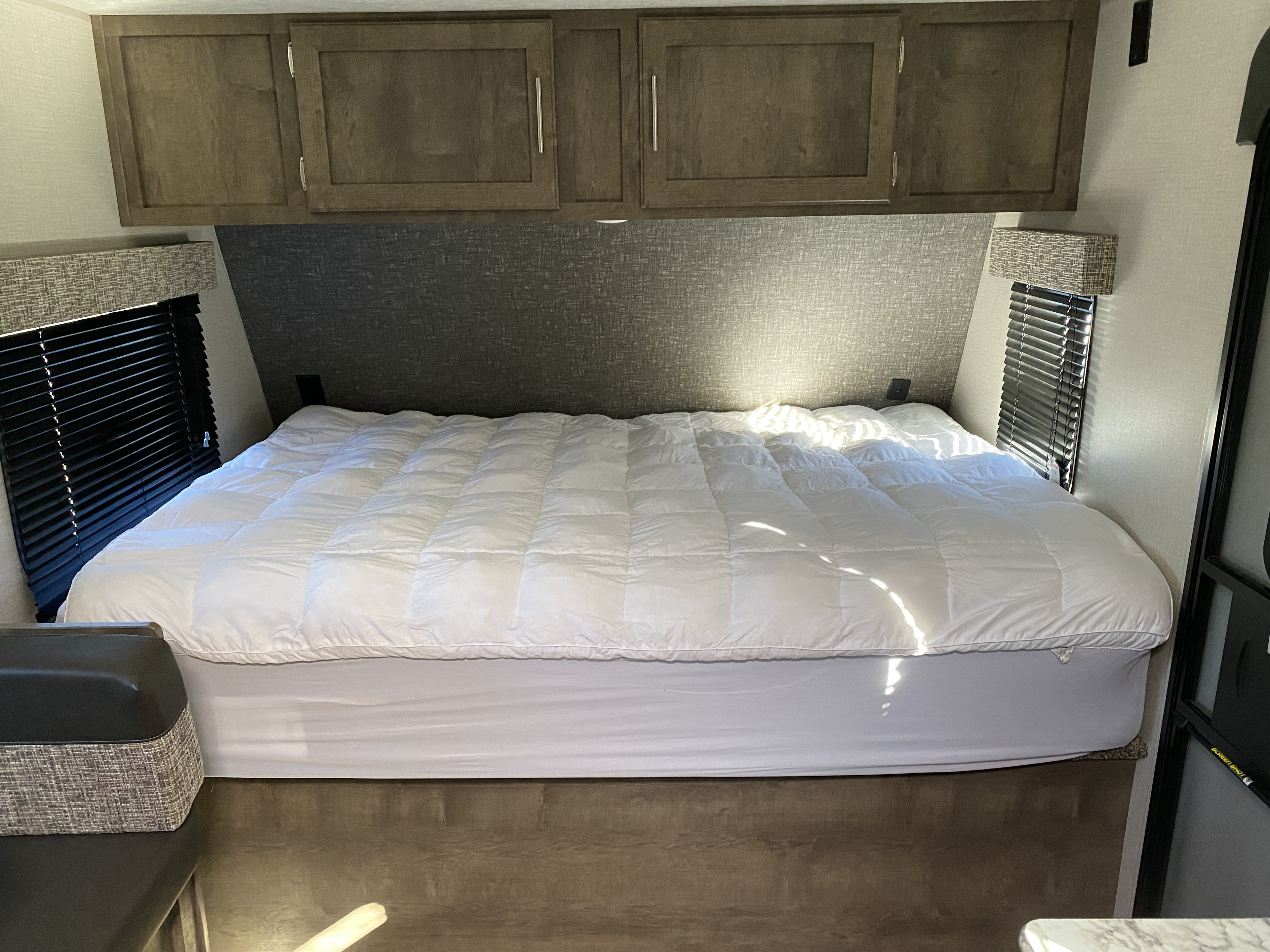 RV rental bedroom interior features a plush bed, overhead cabinets, and side windows with blinds for a cozy stay.. KZ Sportsman 2020