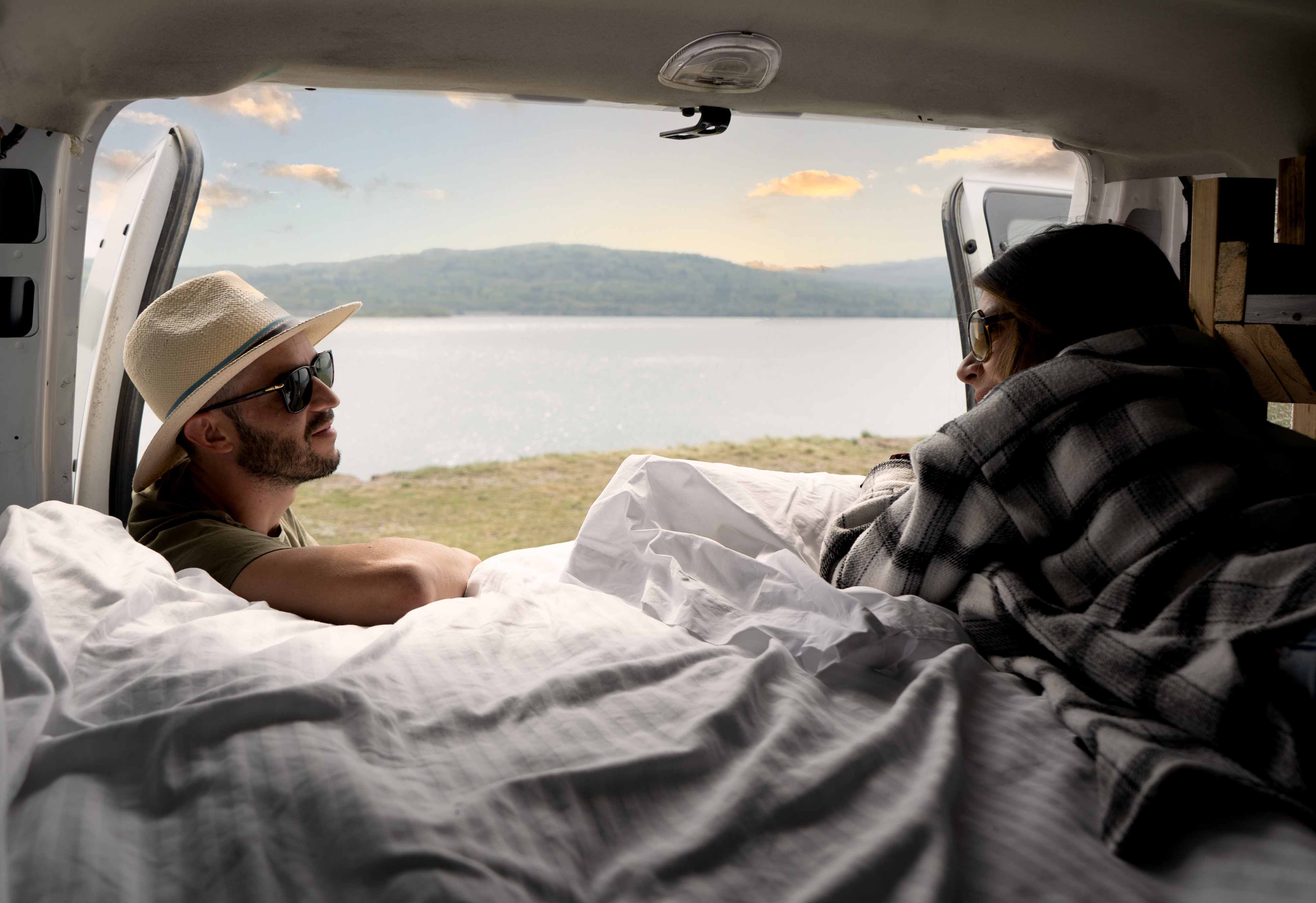 Cozy RV rental setup: a couple relaxes inside, gazing at a serene lake and mountains through the open back of their van.. Glacier Campers Eco Camper 2012