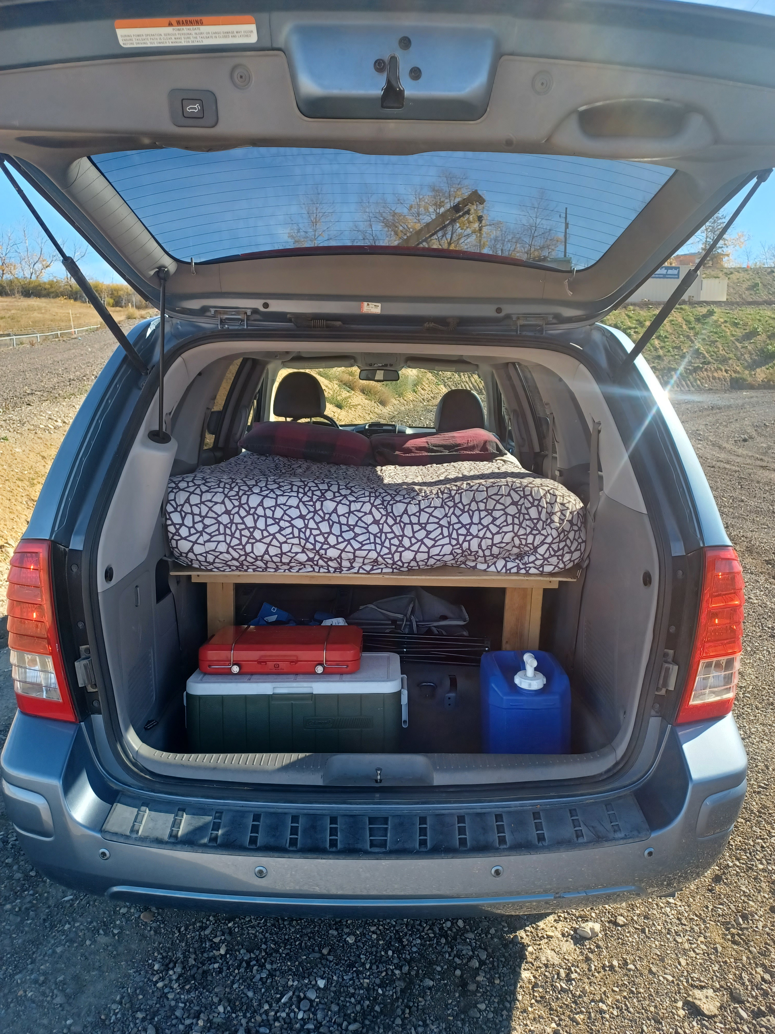 Open SUV tailgate reveals an "RV rental"-style car camping setup with a bed platform, cooler, and water storage.. Glacier Campers Eco Camper 2012