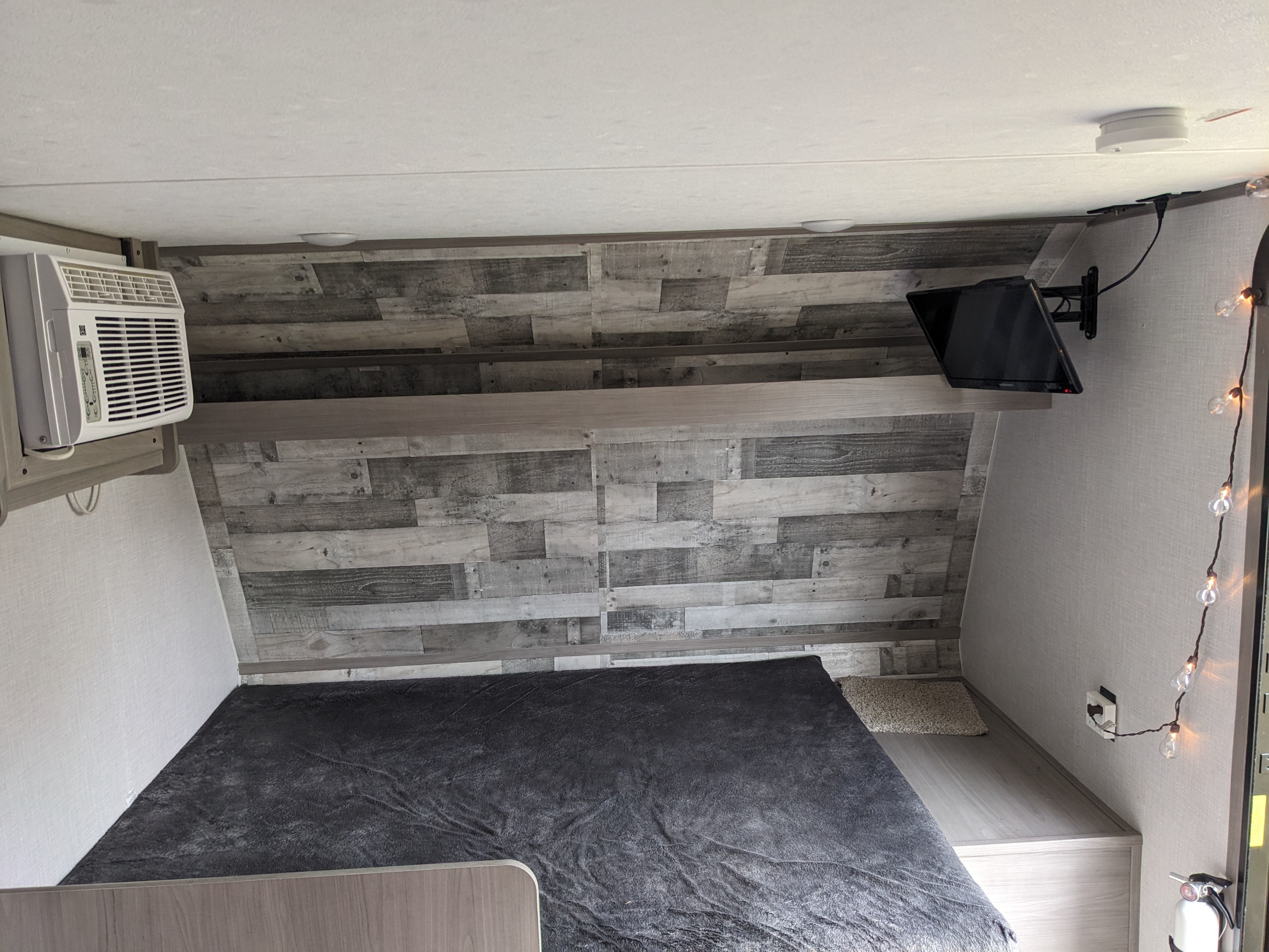 RV rental bedroom: Features a wall AC unit, mounted TV, and a cozy bed against wood-paneled walls.. Dutchmen Coleman Lantern 2023