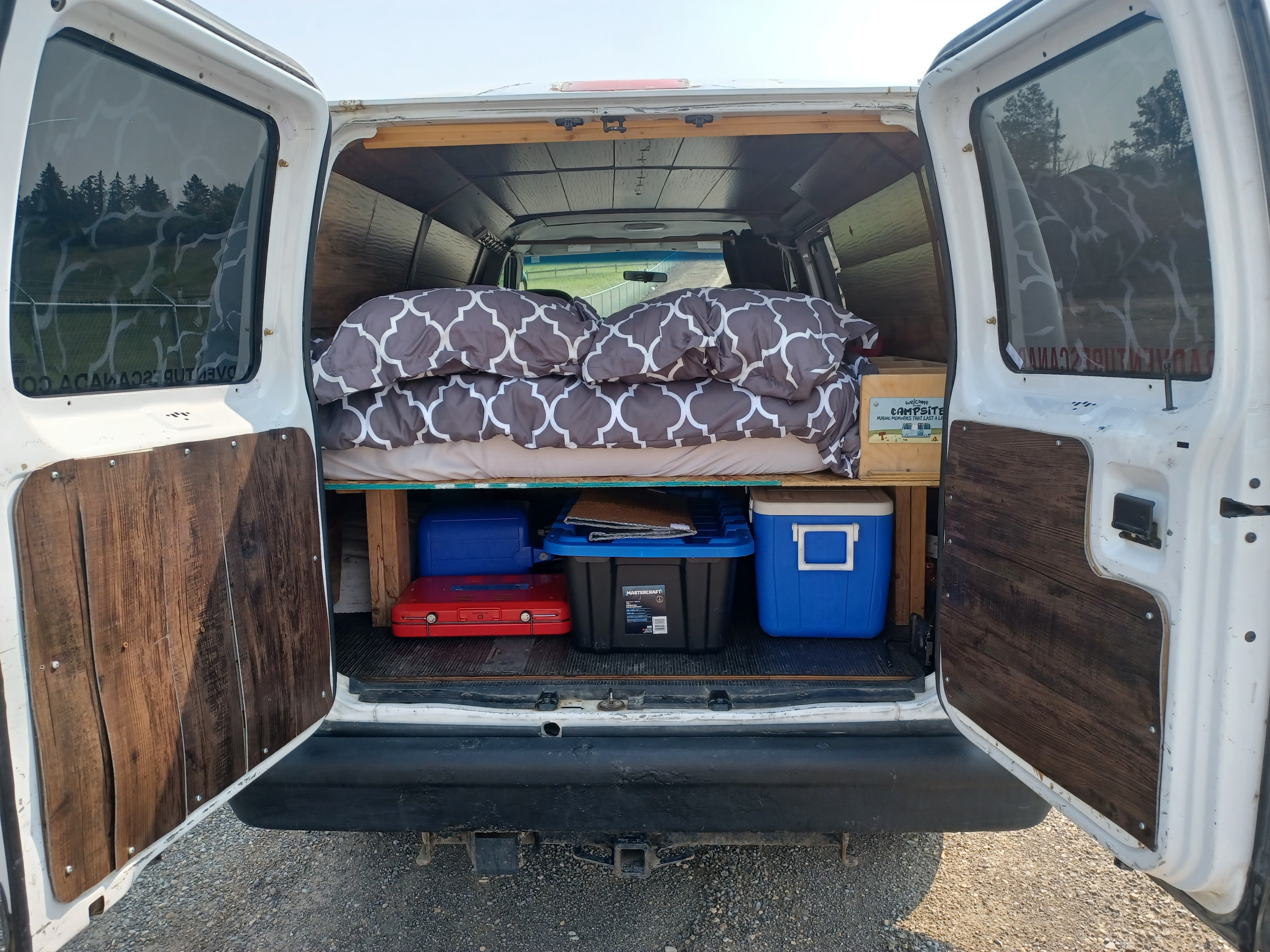 Rear view of a cozy custom camper van interior for RV rental, featuring a bed, ample storage, and wood accents.. Glacier Campers #Vanlife Camper 2014