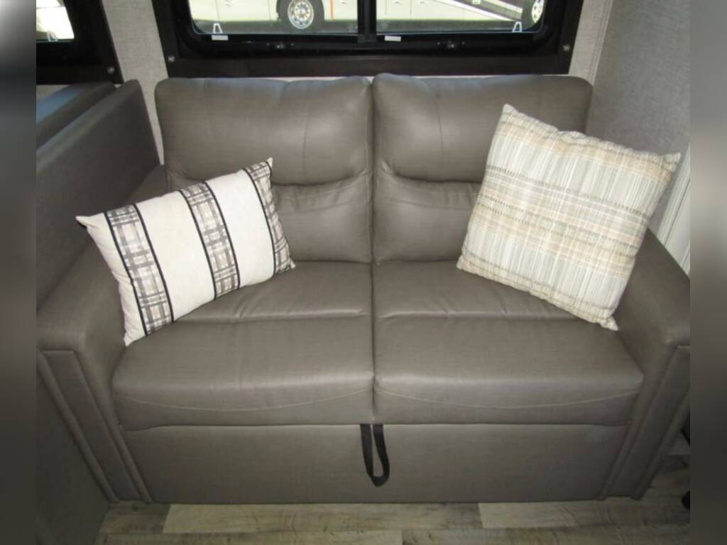Inside this RV rental, find a comfortable gray pull-out sofa with two decorative plaid cushions, perfect for relaxing or sleeping.. Jayco Redhawk 2022