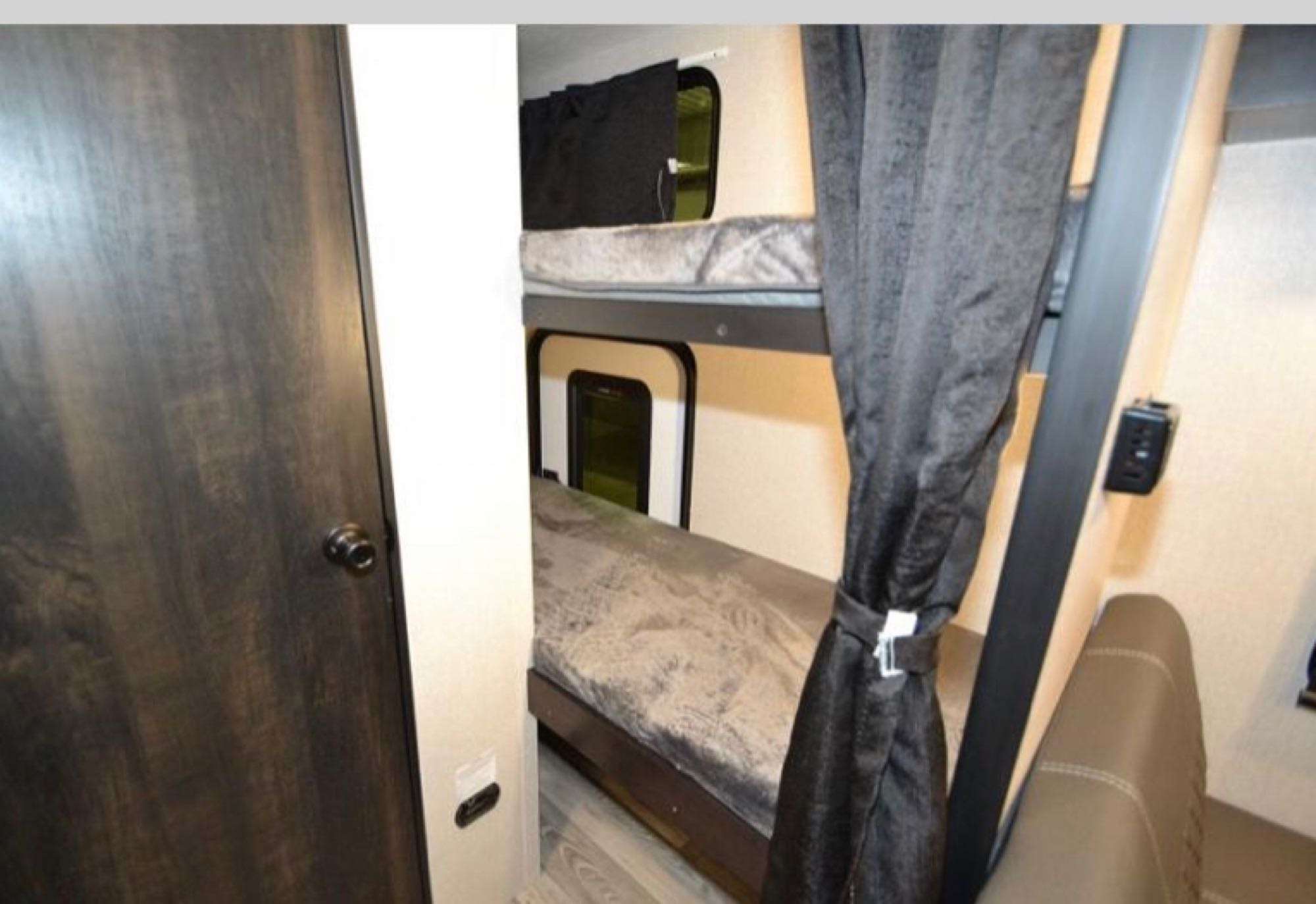 RV rental interior featuring two stacked bunk beds with windows and privacy curtains, alongside a dark wood door.. Starcraft Super Lite Maxx 2022