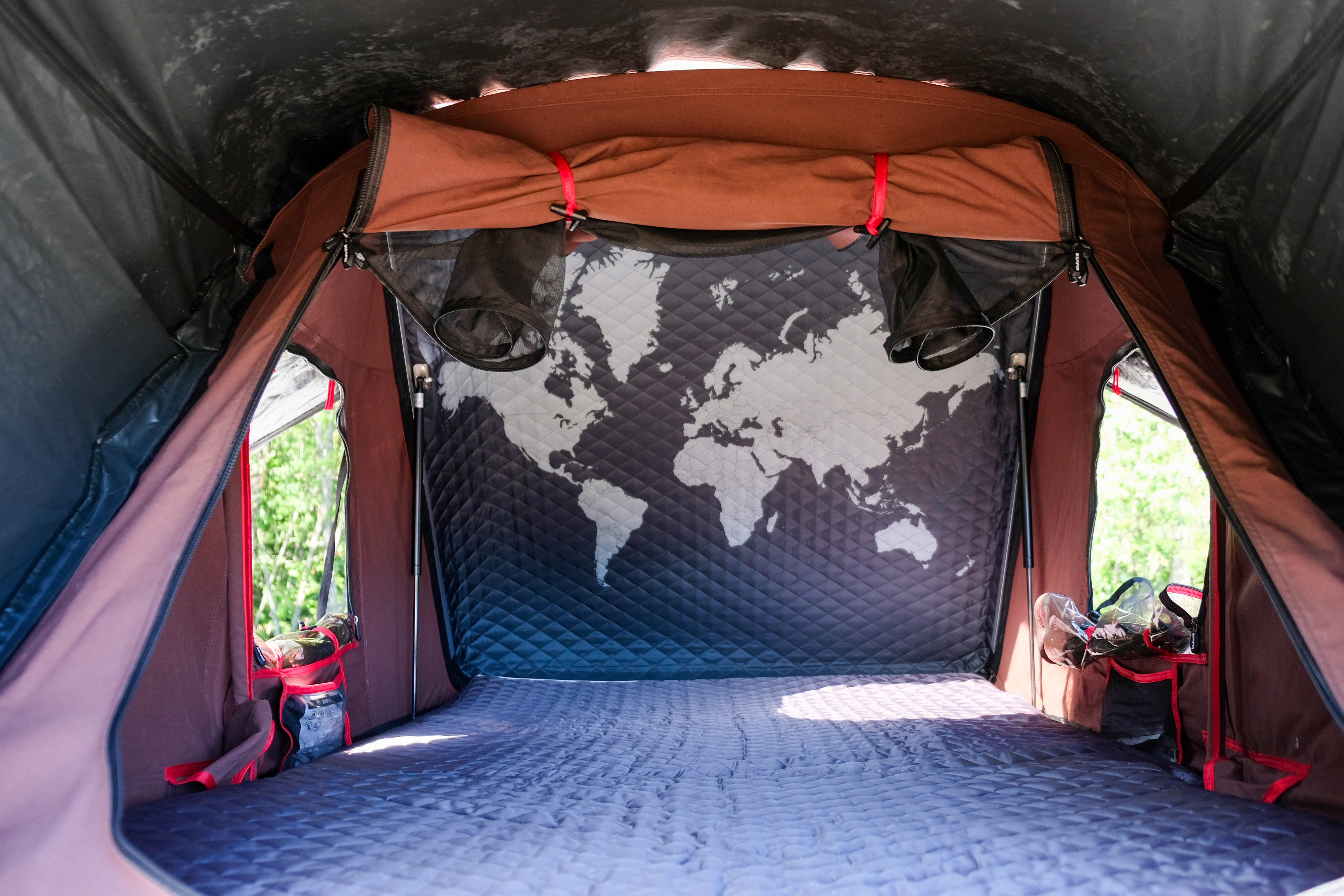 Inside an RV rental rooftop tent: quilted bed, world map back wall, and mesh storage. Ready for your camping journey.. Subaru Outback Wilderness 2023