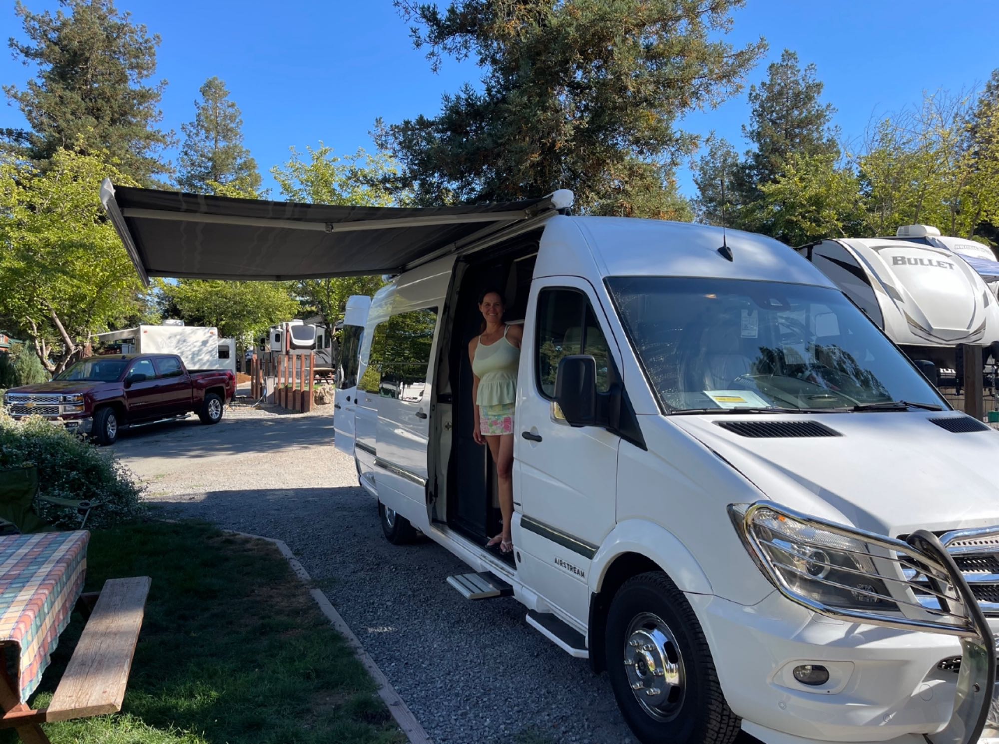 Woman stands in an Airstream RV rental with awning extended at a sunny campground. Perfect for your next road trip!. Airstream Interstate 2015
