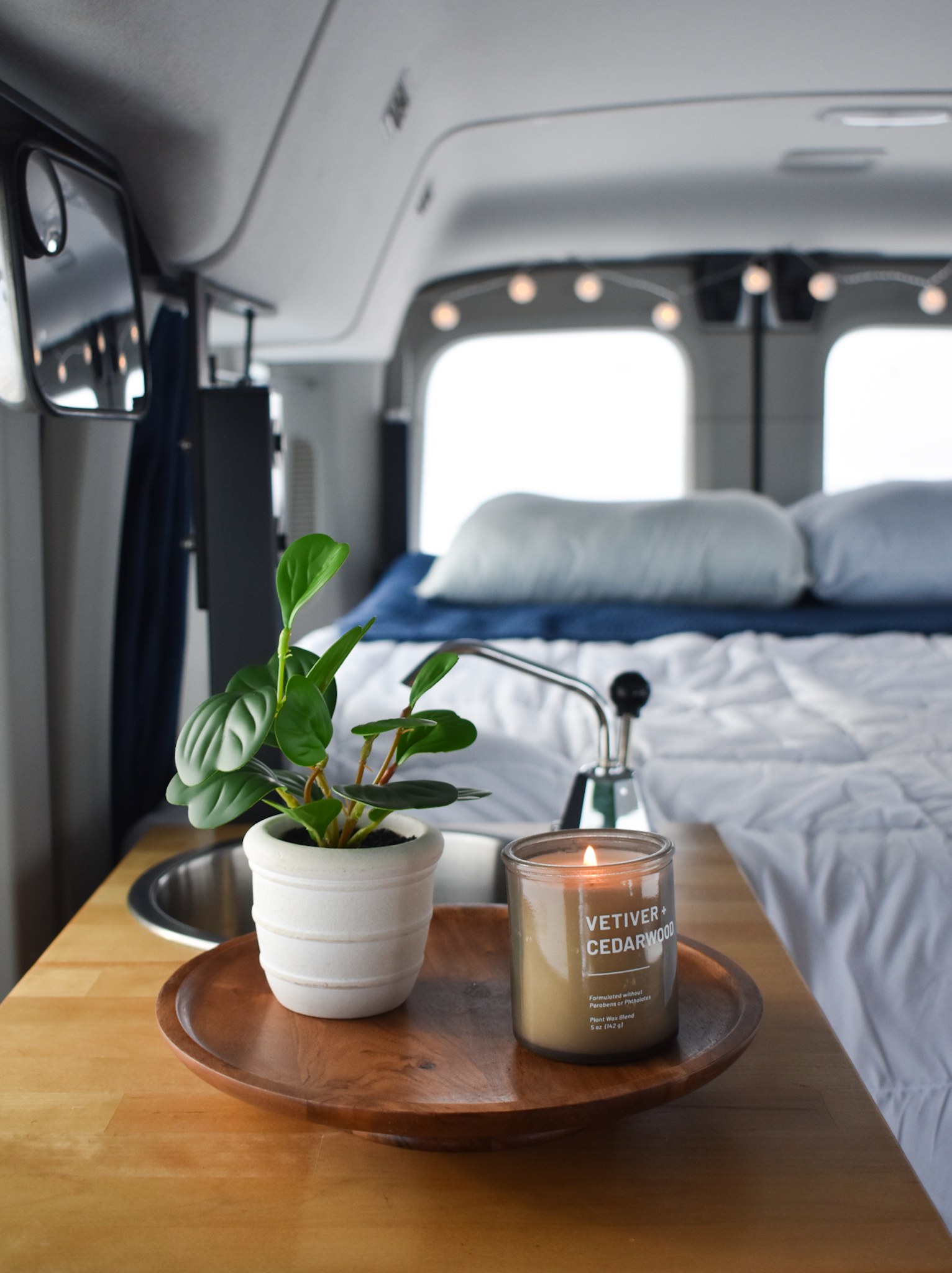 Cozy rv rental interior: Potted plant, lit Vetiver+Cedarwood candle on wood, sink, and a comfy bed.. Ford Van 2016