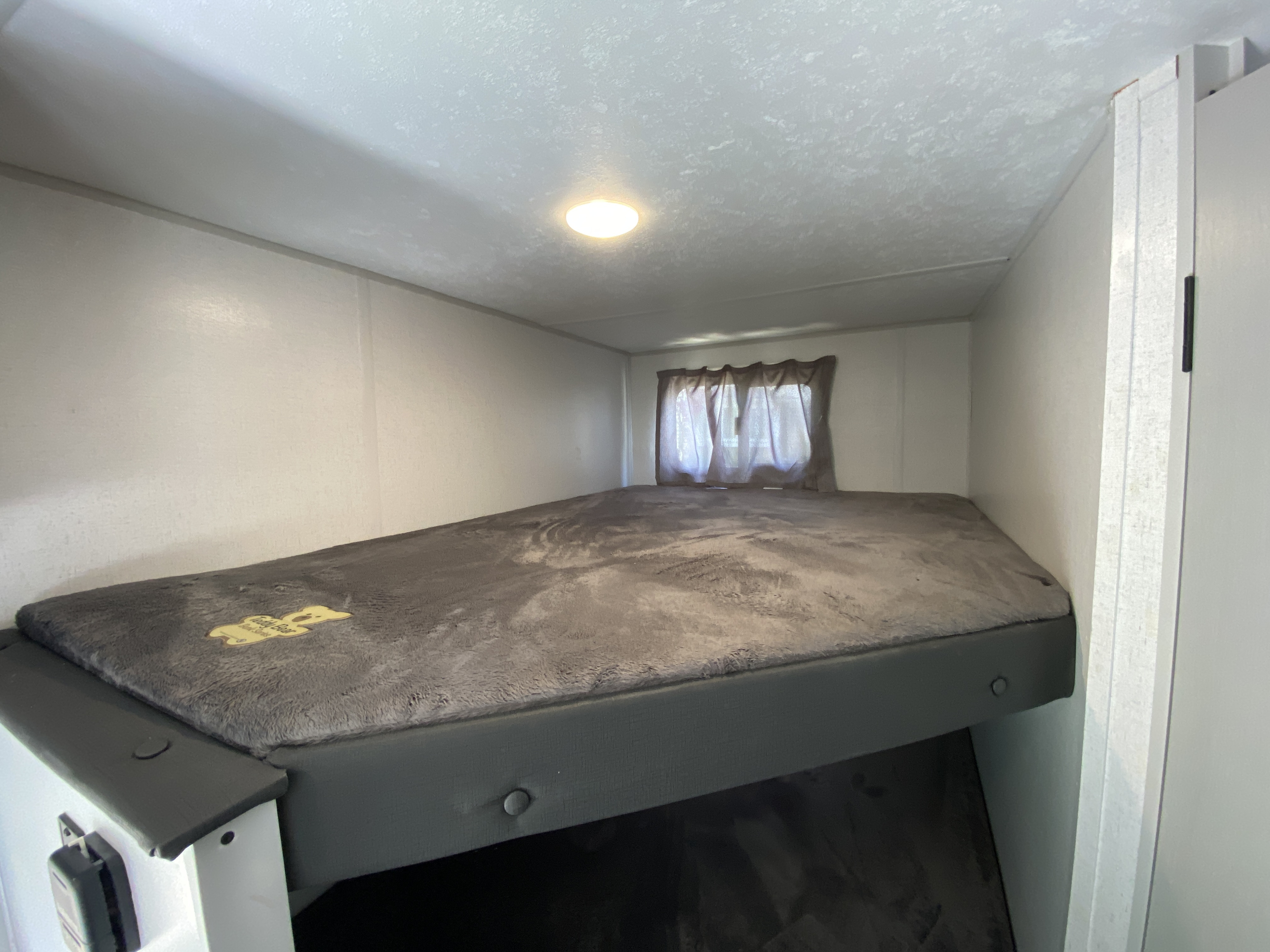 Cozy RV rental bunk bed, complete with soft grey blanket, window, and ceiling light. Perfect sleeping area.. Forest River Salem FSX 2021