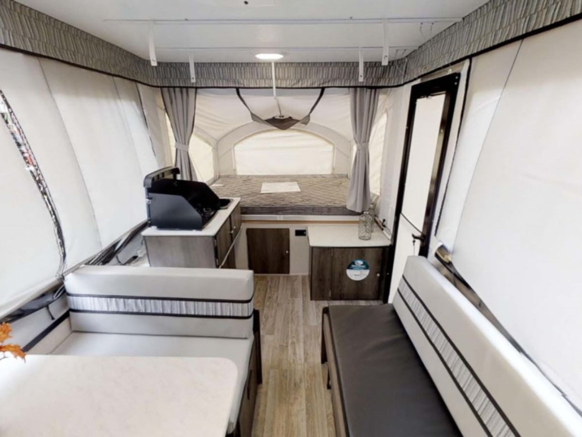 Inside a modern pop-up camper RV rental: dinette, stove on counter, and a rear bed. Bright, compact travel space.. Coachmen Clipper 2023