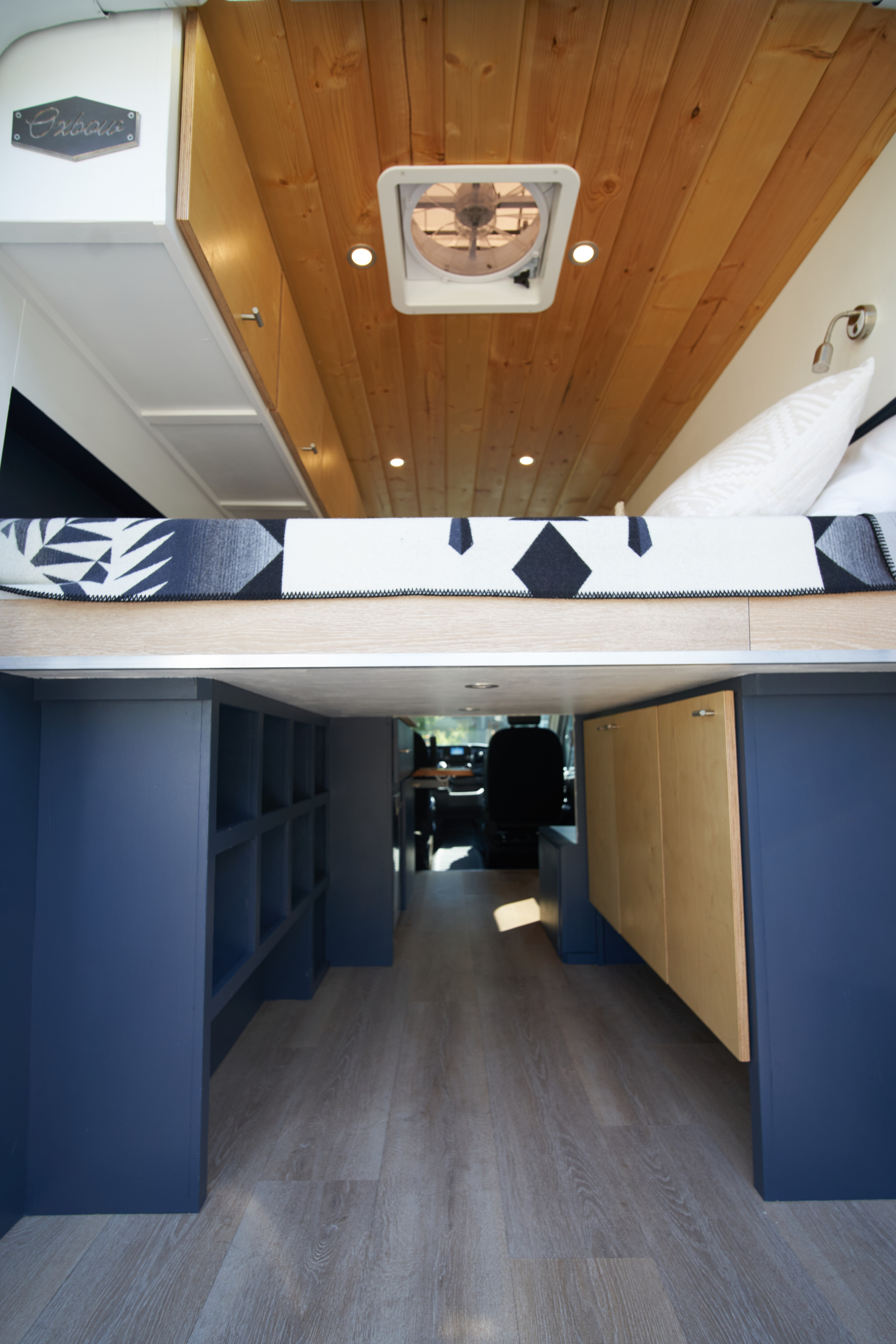 Experience this stylish RV rental! Elevated bed, wood ceiling, ample dark blue storage, and light flooring create a cozy mobile home.. Ford Transit 2021