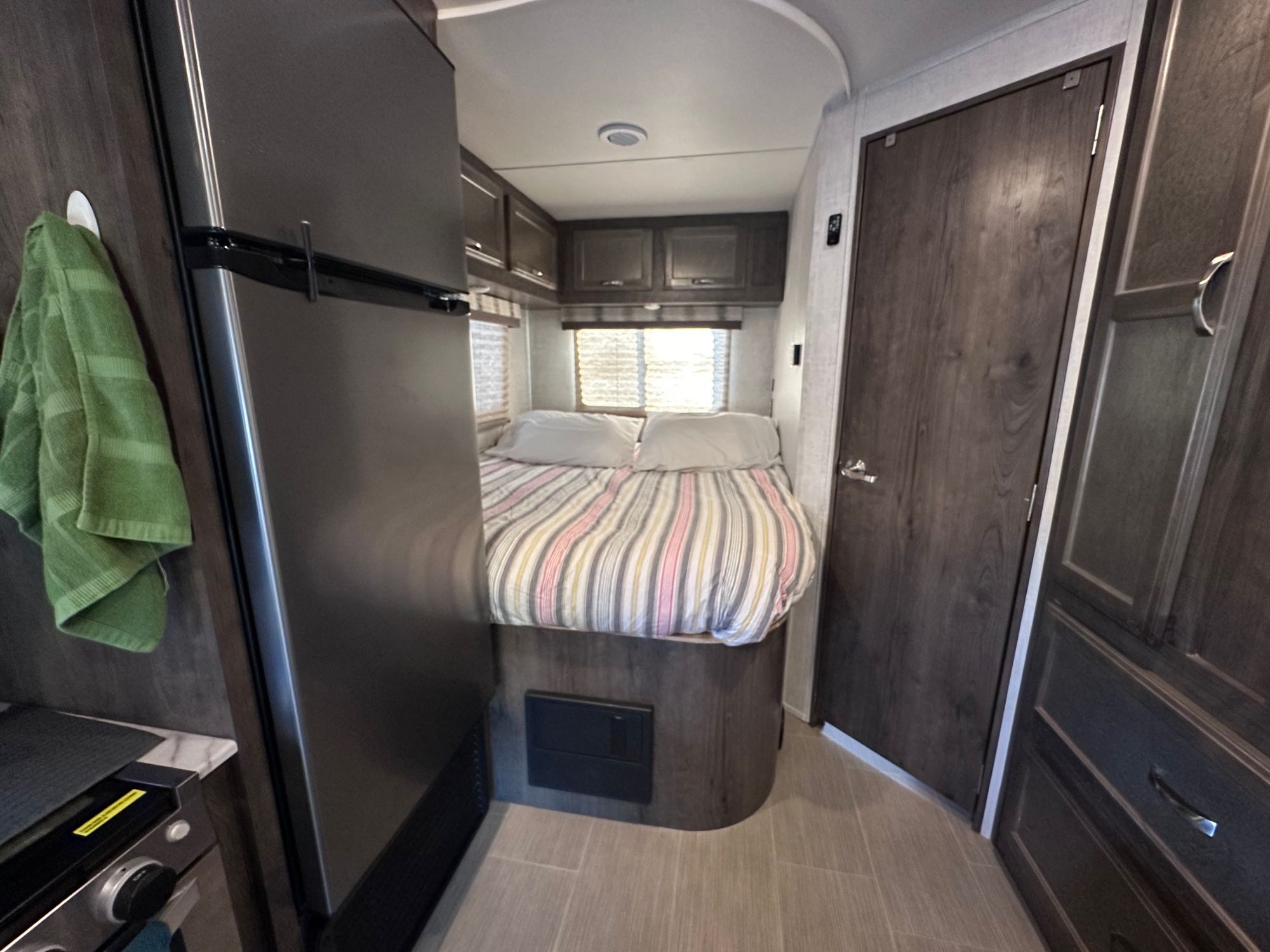 Inside an RV rental: a compact bedroom with a bed, overhead cabinets, and a refrigerator.. Gulf Stream Conquest 2021