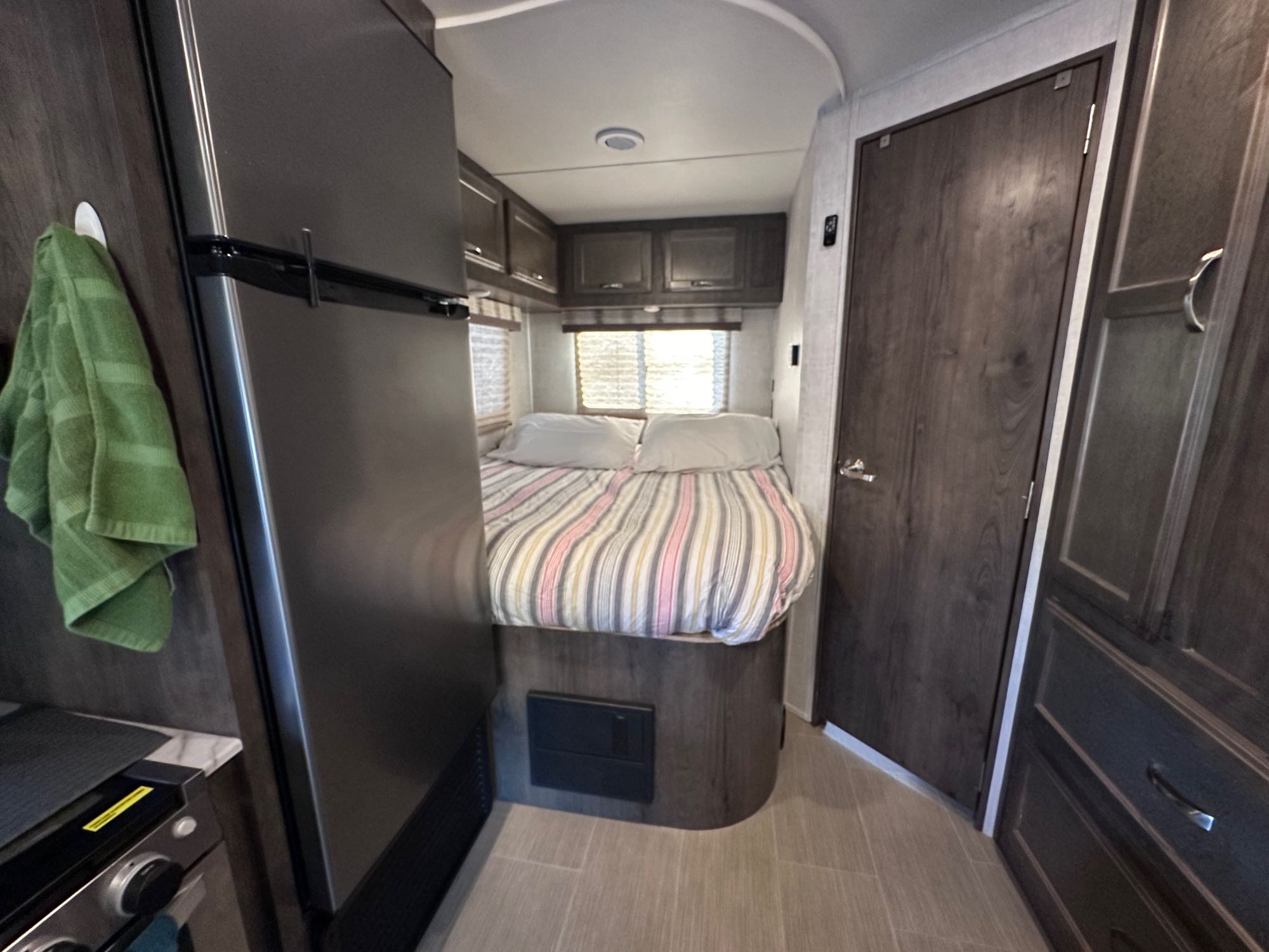RV rental interior: view of the bed with striped bedding, a dark refrigerator on the left, and dark wood cabinetry.. Gulf Stream Conquest 2021