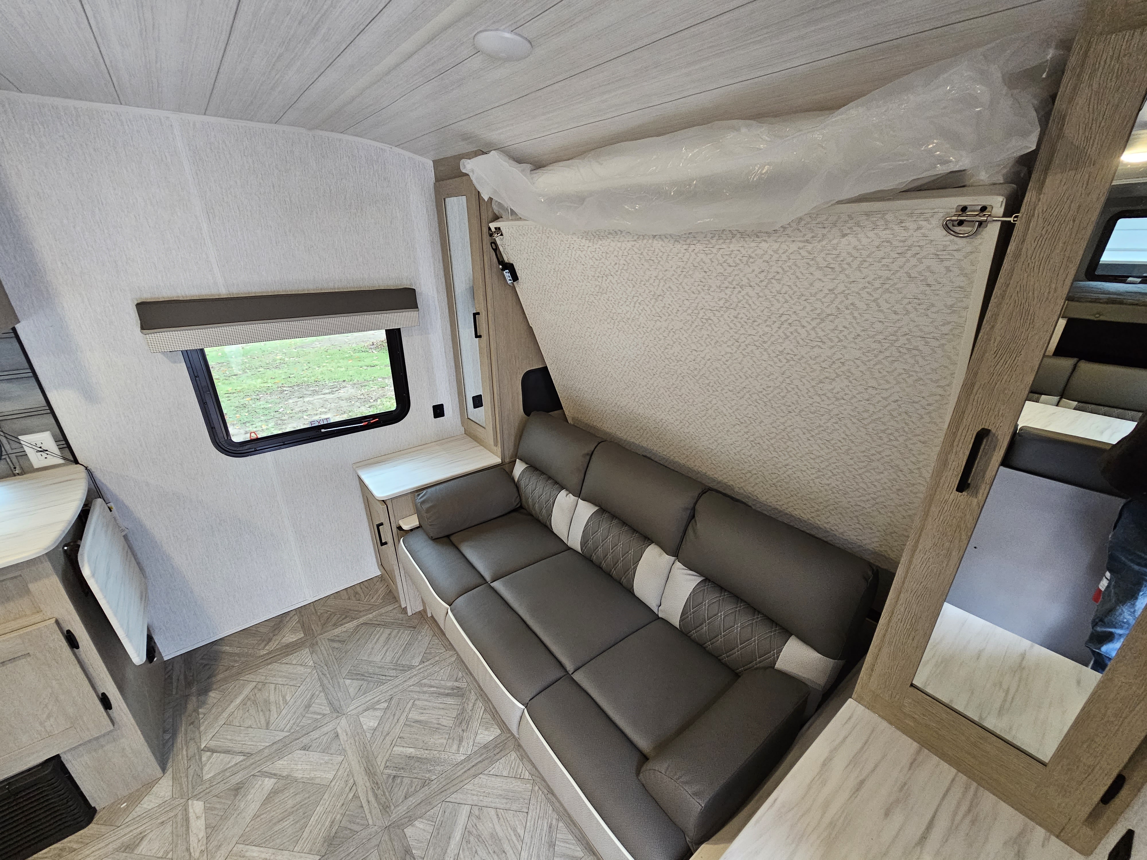RV rental interior showcases a sofa, window, patterned flooring, and a space-saving fold-down bed overhead.. Forest River Wildwood X-Lite Platinum 2023