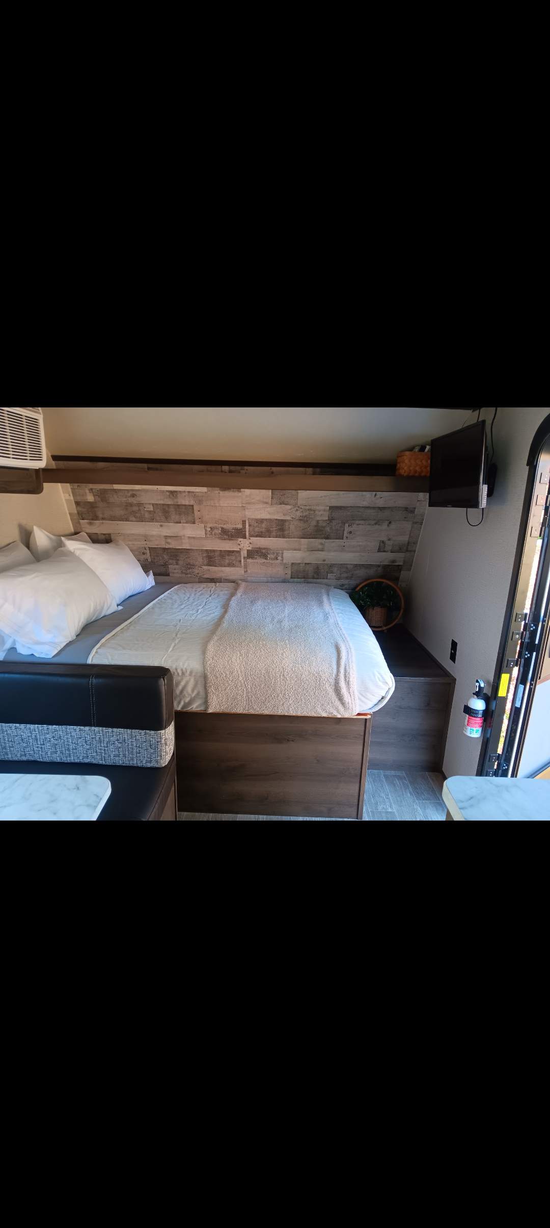 Explore this cozy RV rental interior: a comfortable bed, stylish wood-paneled headboard, and compact dinette.. Dutchmen Coleman Lantern LT 2021